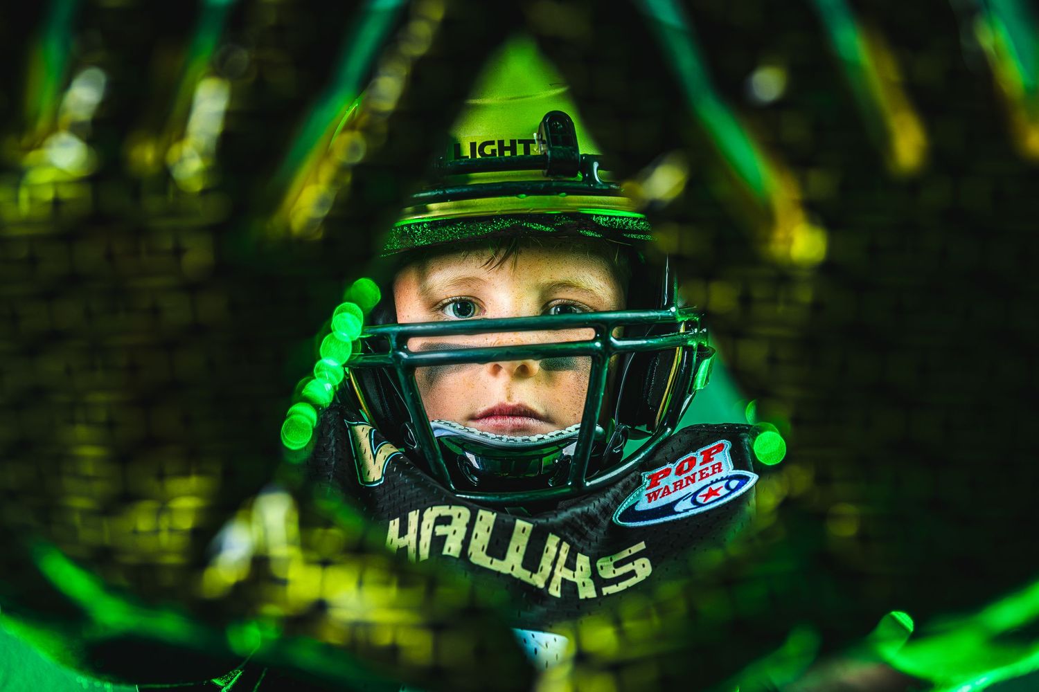 Close up sports portrait with green neon lighting and protective helmet gear showing intense athletic focus.
