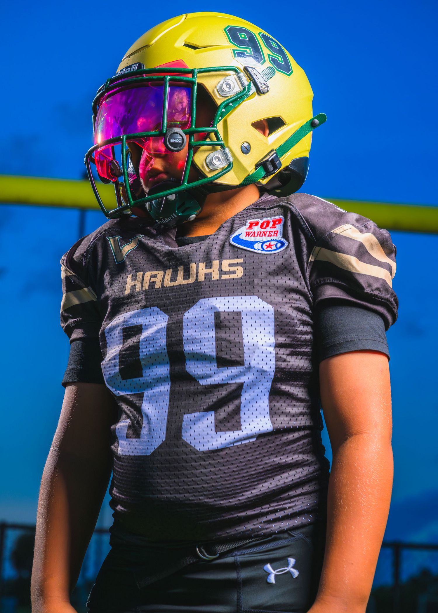 Close-up view of football players in black jerseys with yellow and green helmets against a bright blue sky during practice.