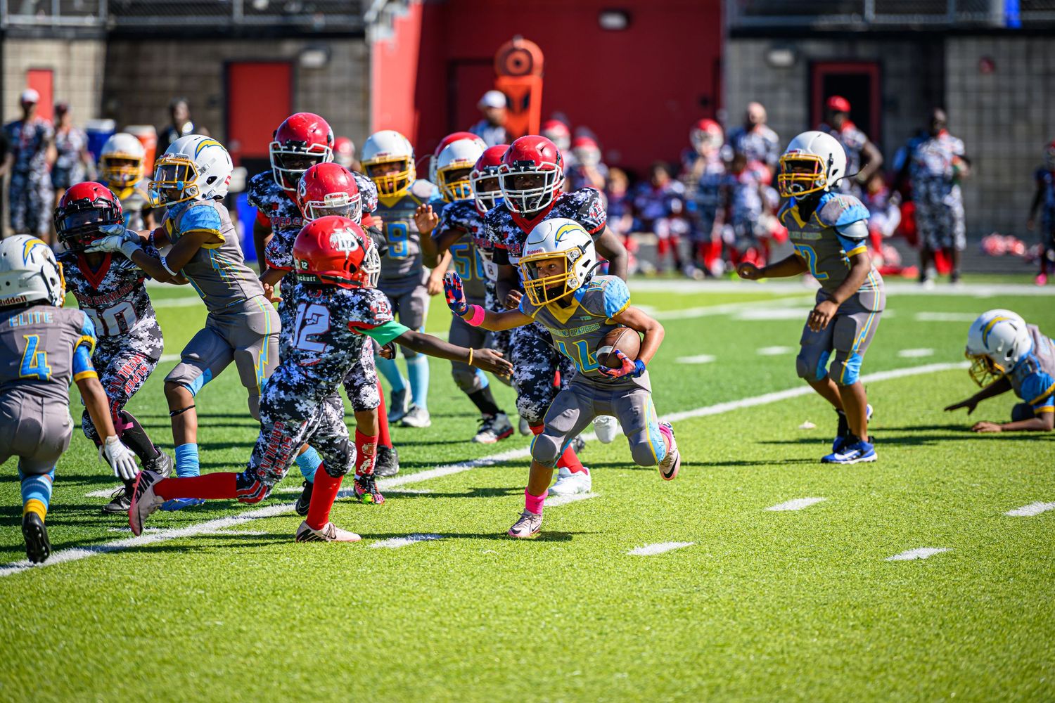 Youth football players in colorful uniforms competing during a game on artificial turf.