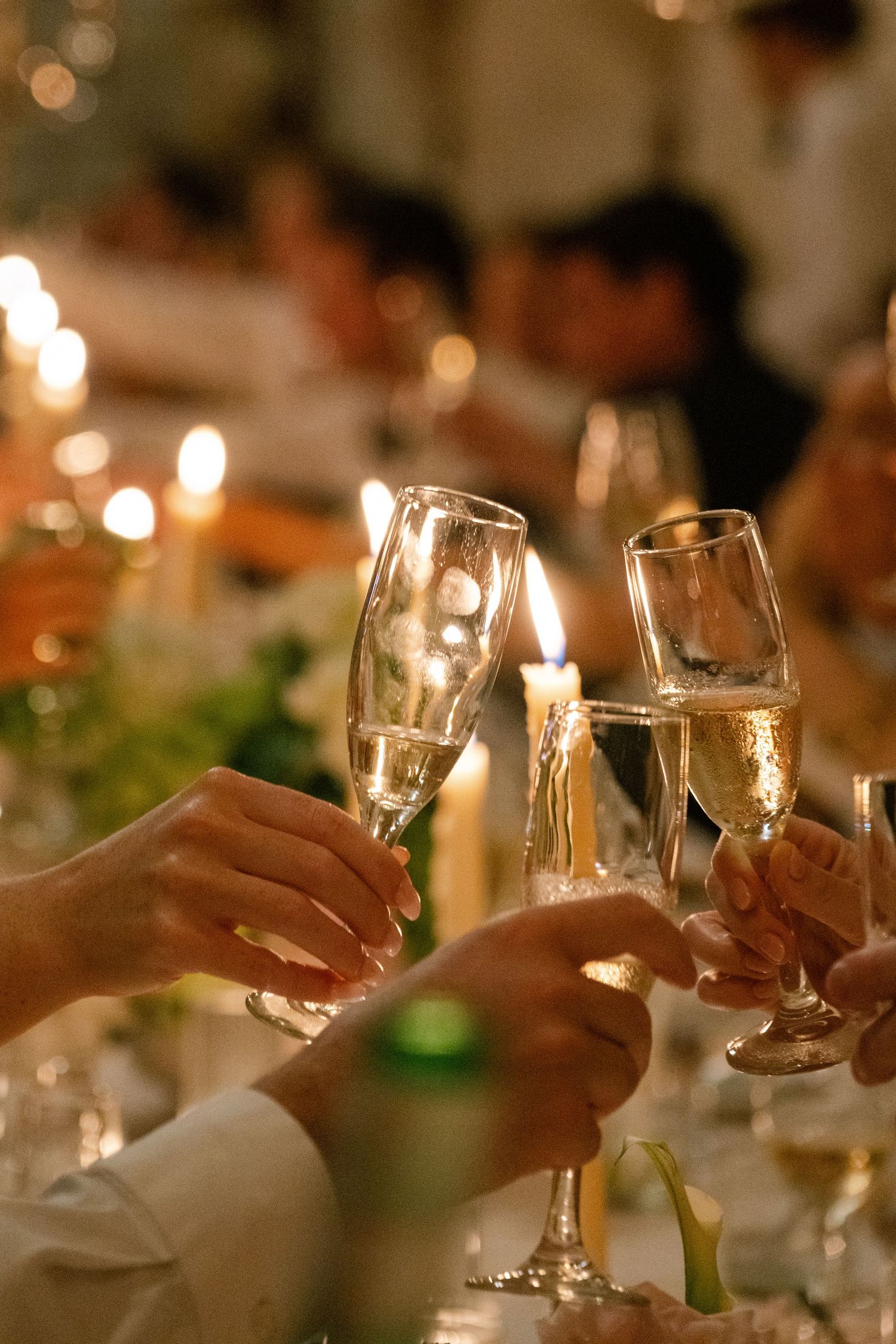 Guests clinking champagne flutes in a toast at an elegant candlelit dinner party celebration.