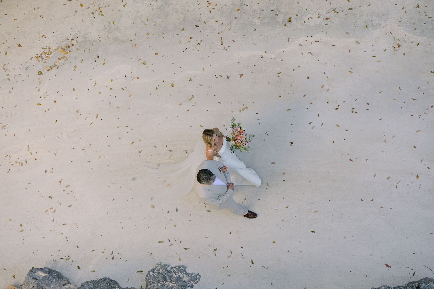 Overhead drone view of couple lying on sandy beach creating heart shape.