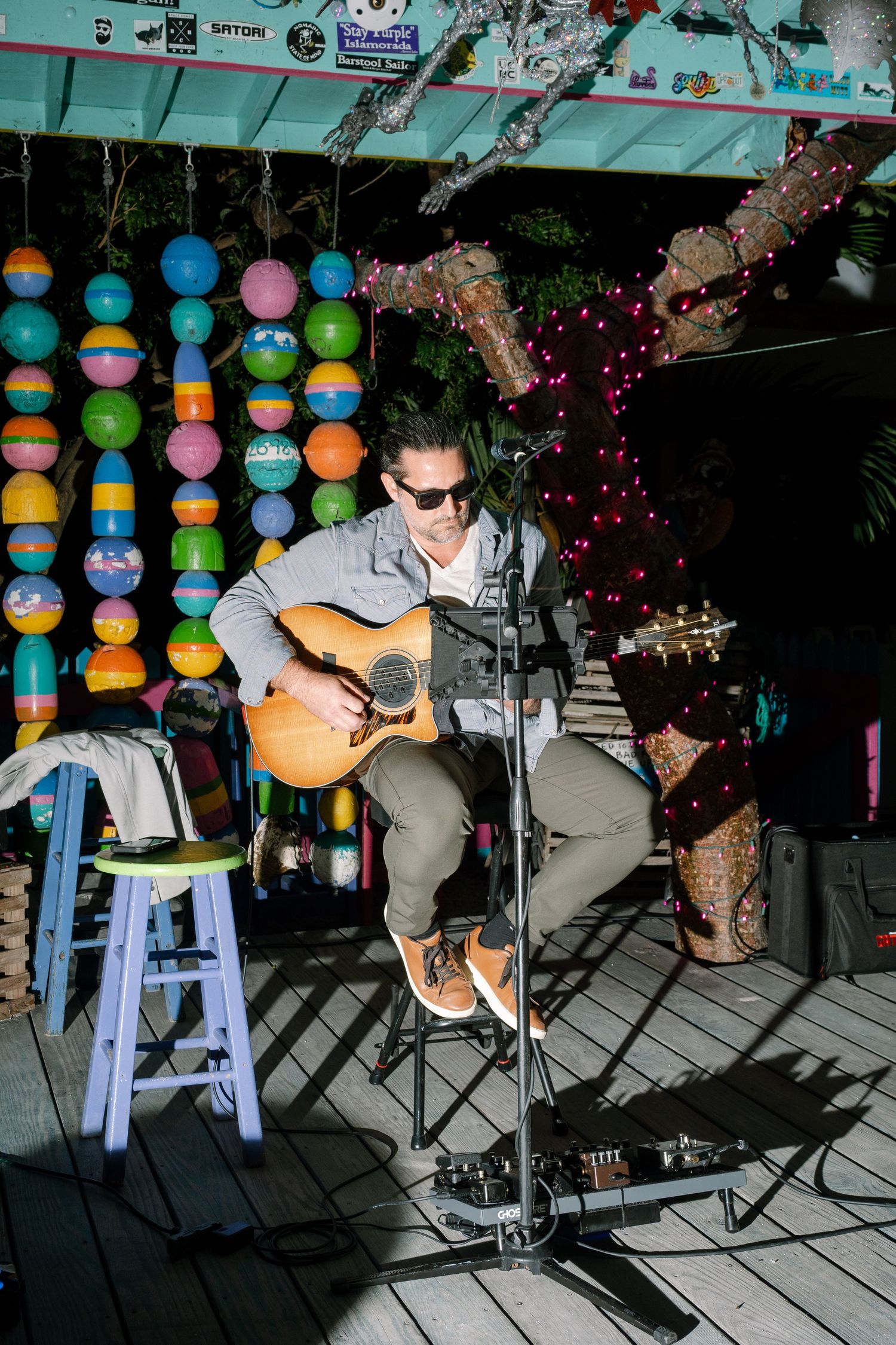 Musician performing on acoustic guitar on outdoor stage with colorful lanterns in background.