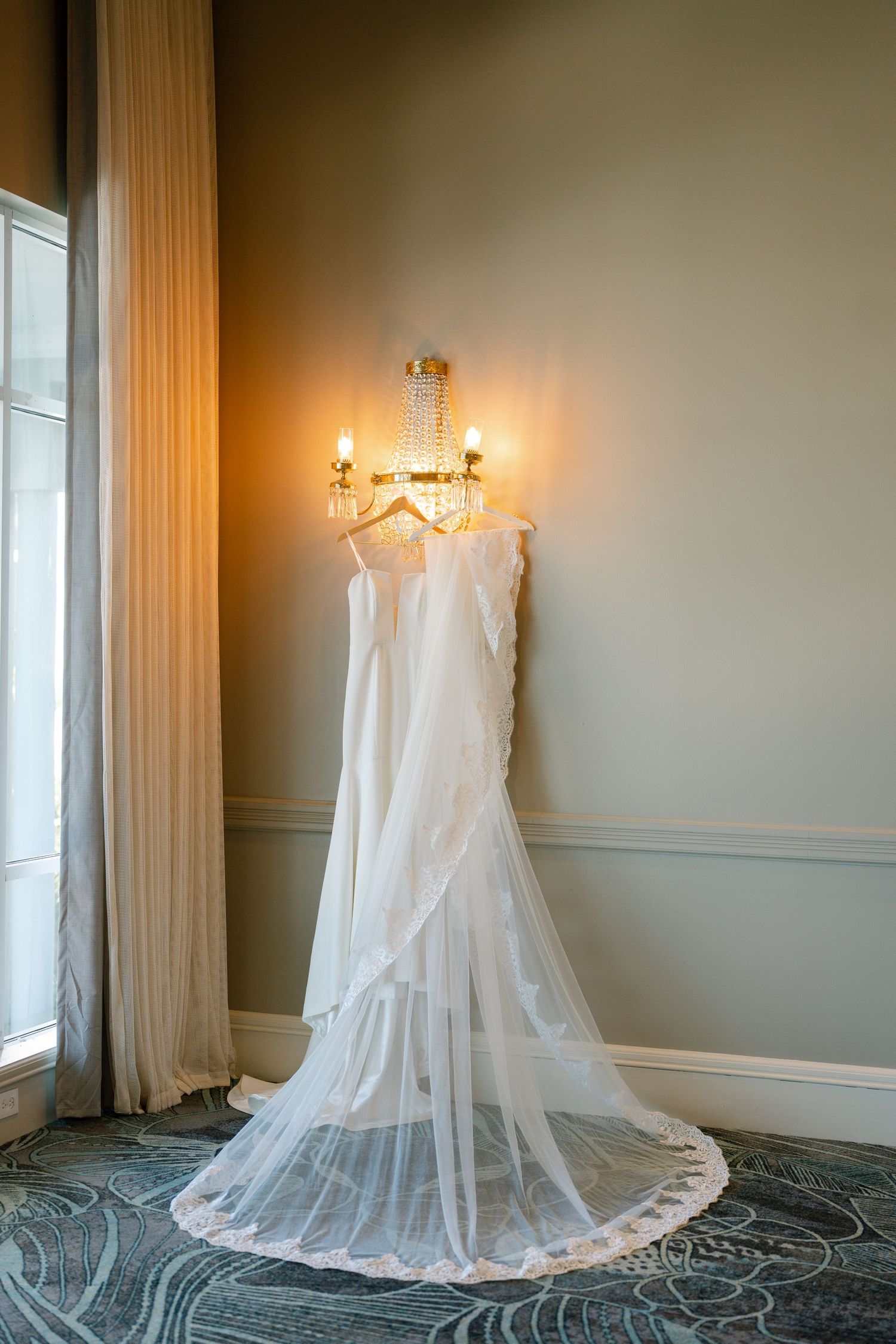 Elegant white wedding dress displayed on a hanger in a softly lit room with classic decor.