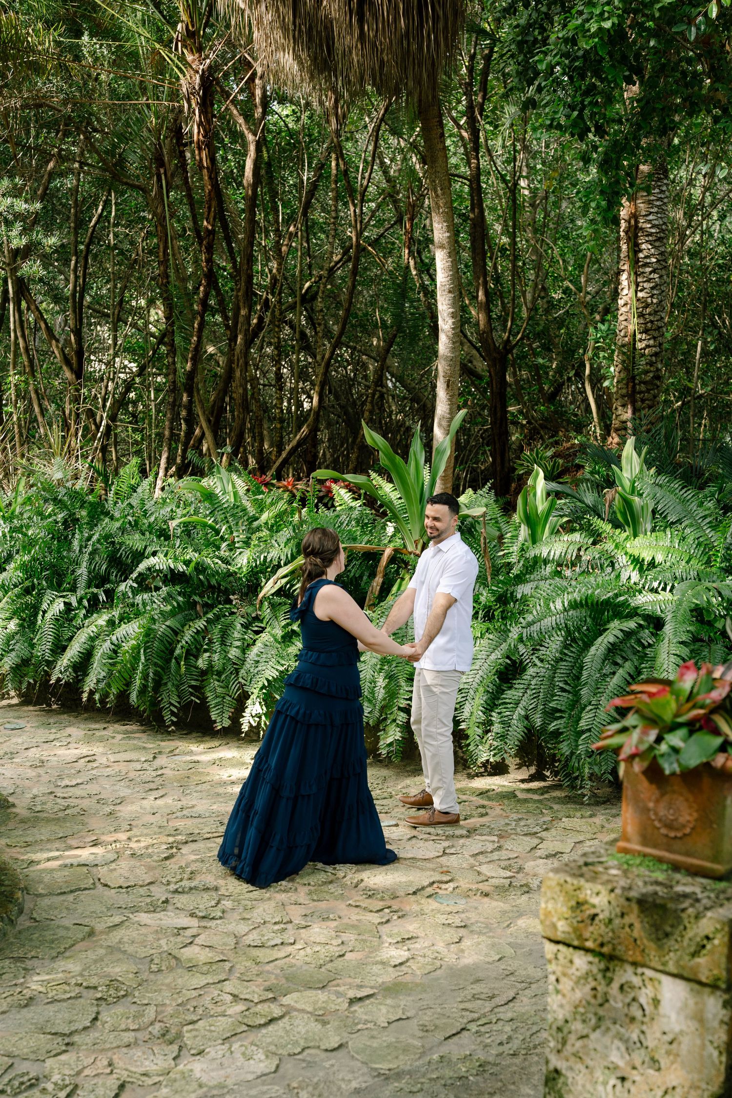 A couple shares a tender moment in a lush garden setting with tropical plants and ferns.