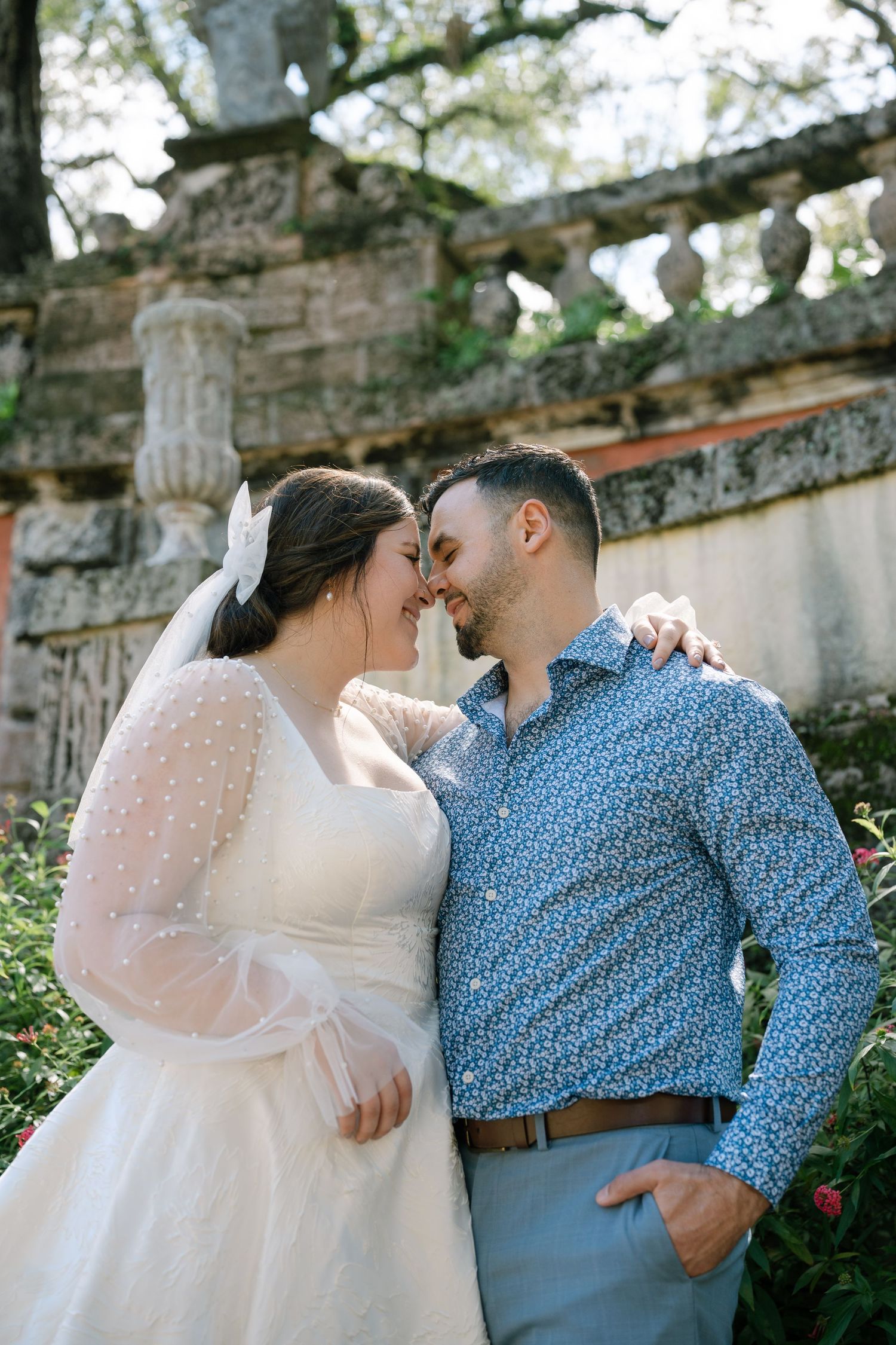 Romantic moment captured against ornate stone architecture in garden setting.