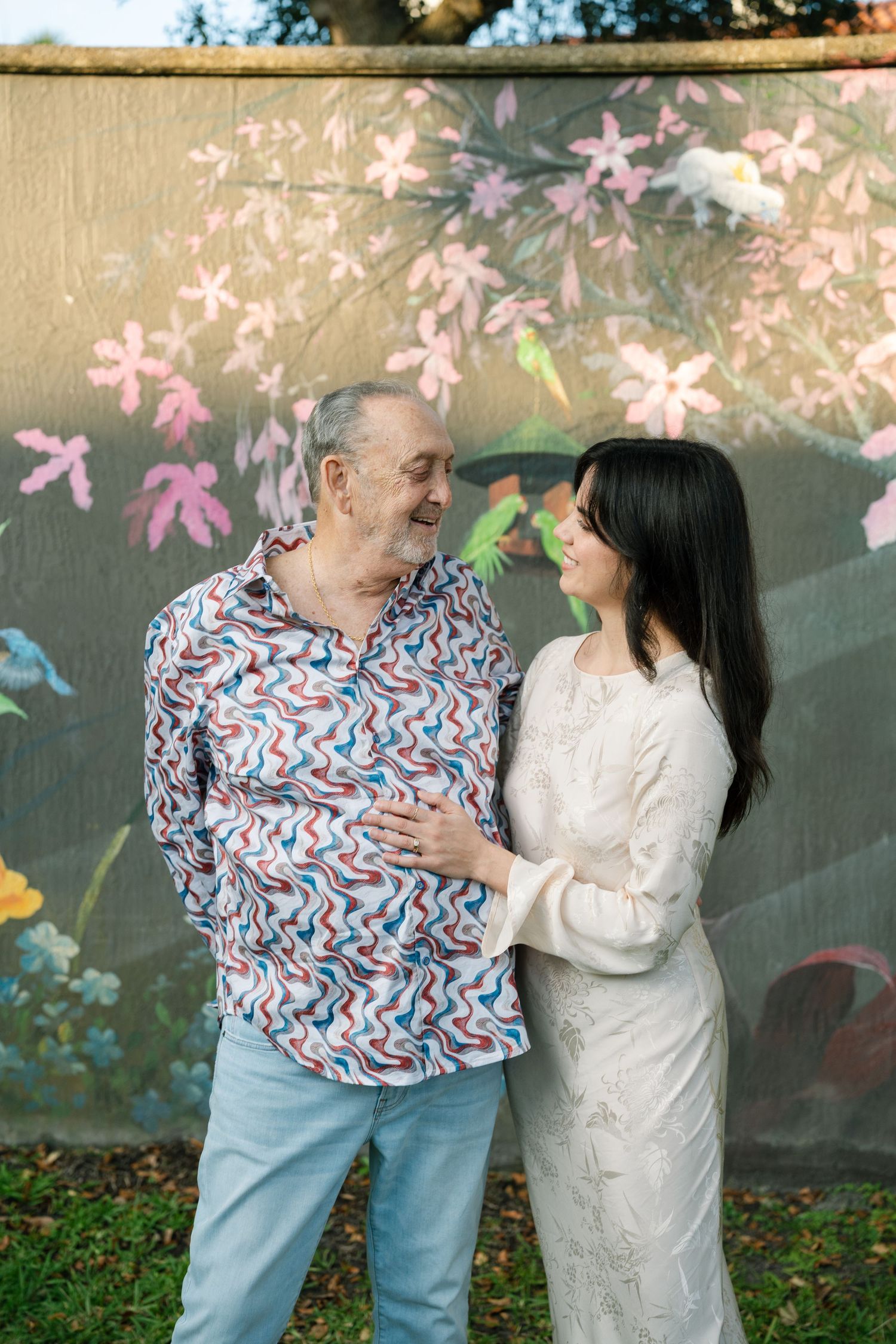 Joyful interaction against floral mural backdrop with pink blossoms and natural lighting.