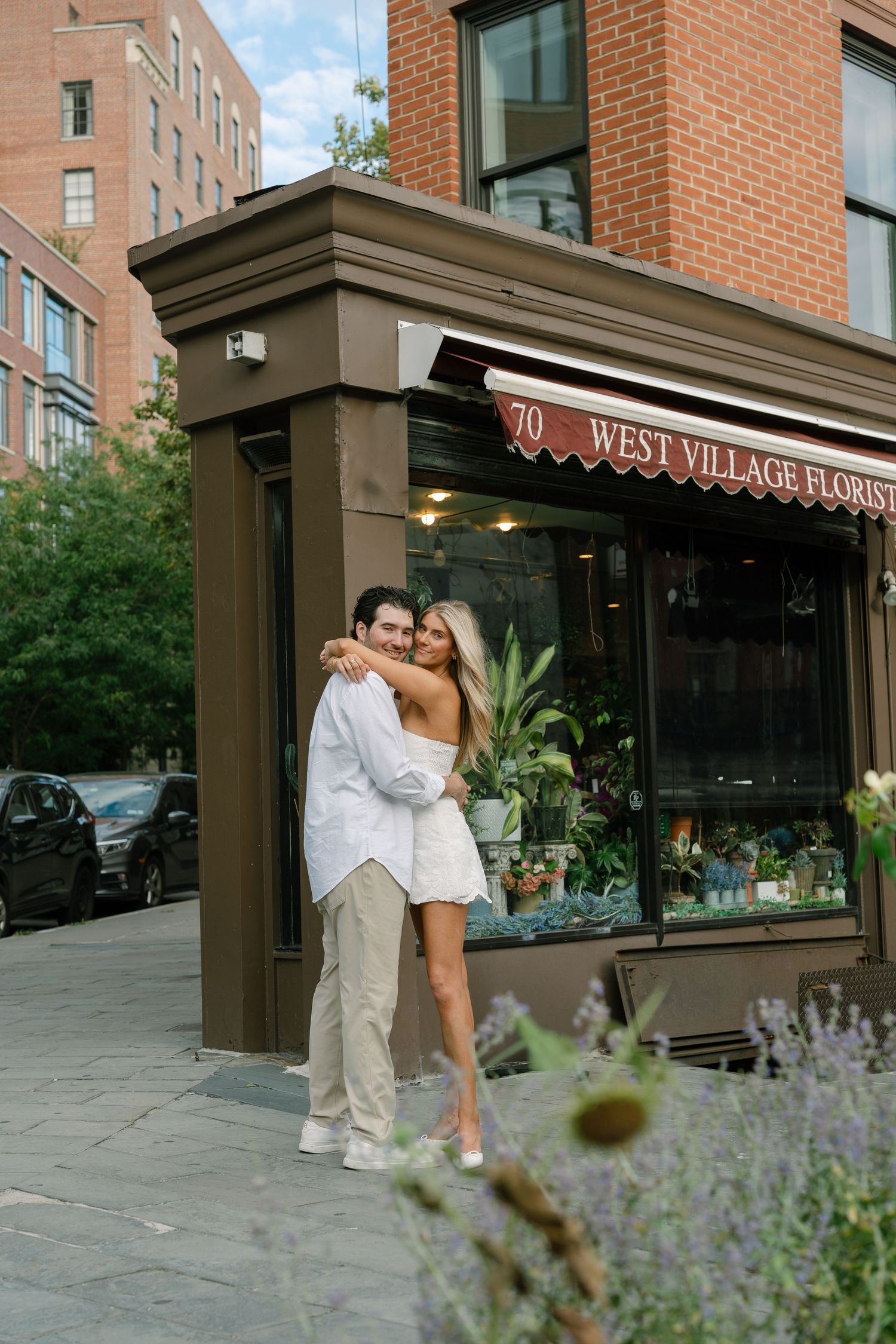 Couple embracing outside West Village Florist shop at 70, woman in white mini dress, man in white shirt, NYC street.