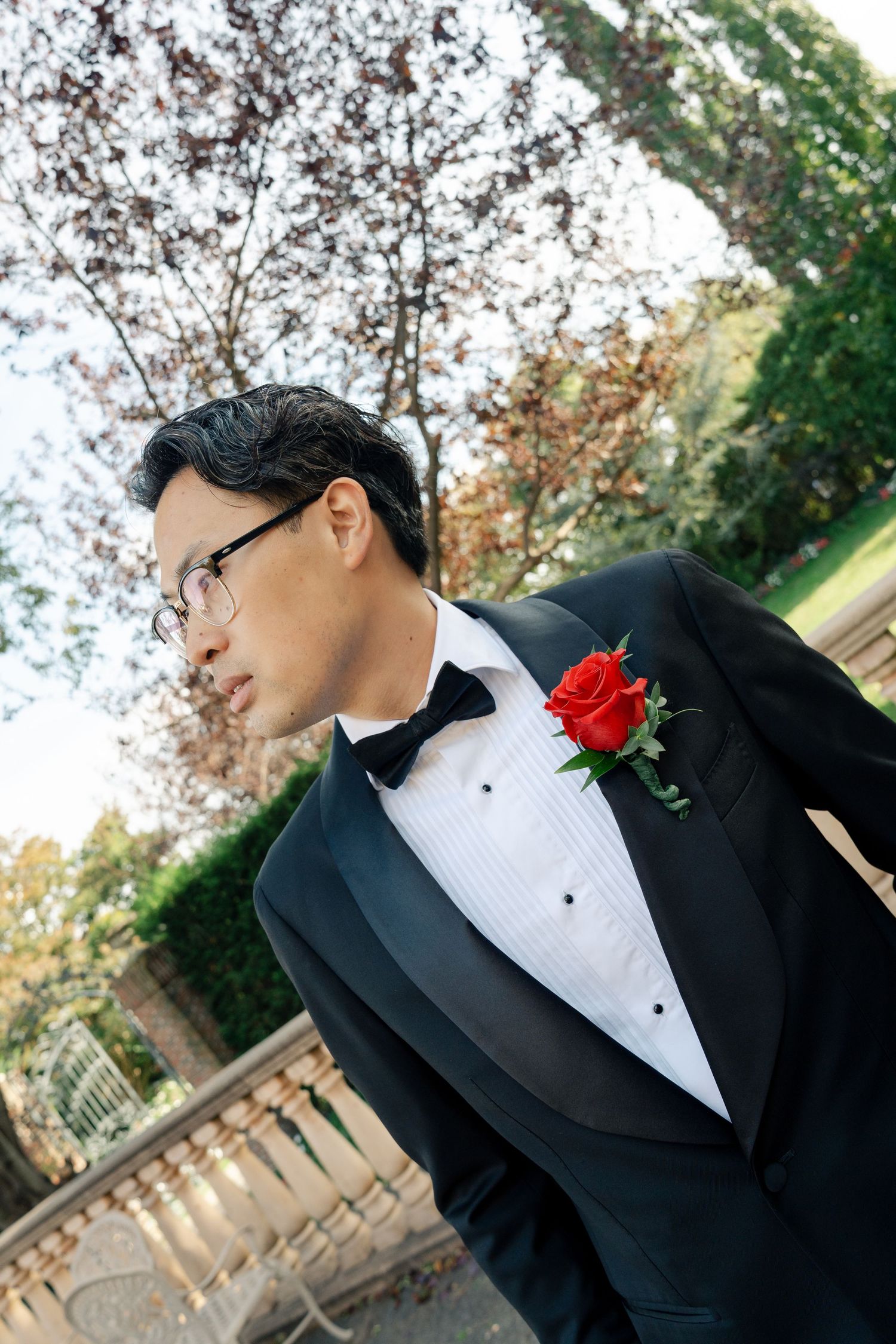 Formal portrait in a garden setting showing details of black tuxedo with red boutonniere.