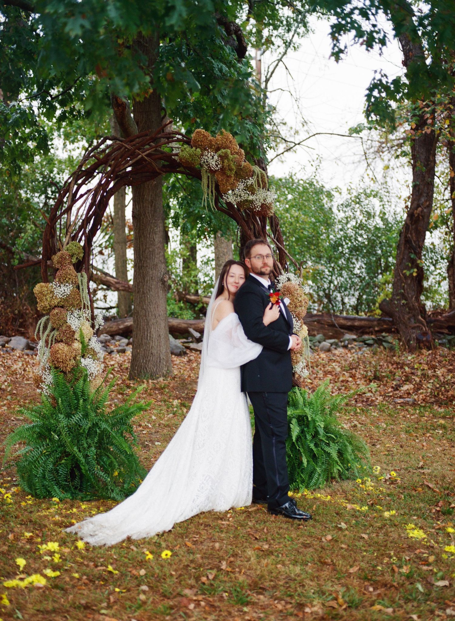 Romantic wedding couple shares intimate moments in a wooded setting with fallen autumn leaves and evergreen ferns.