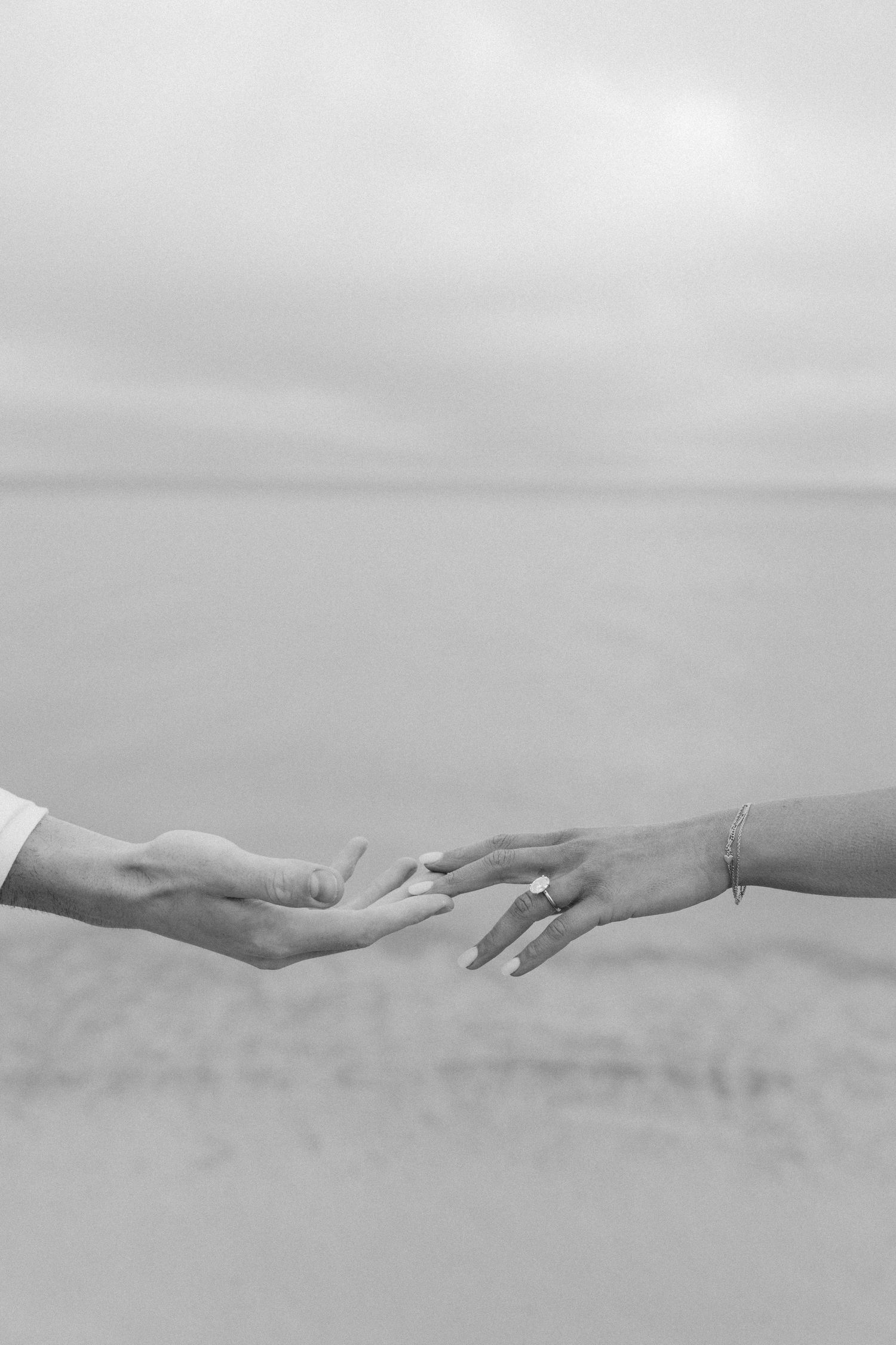 A black and white artistic photograph shows two hands reaching towards each other across a misty, ethereal landscape.