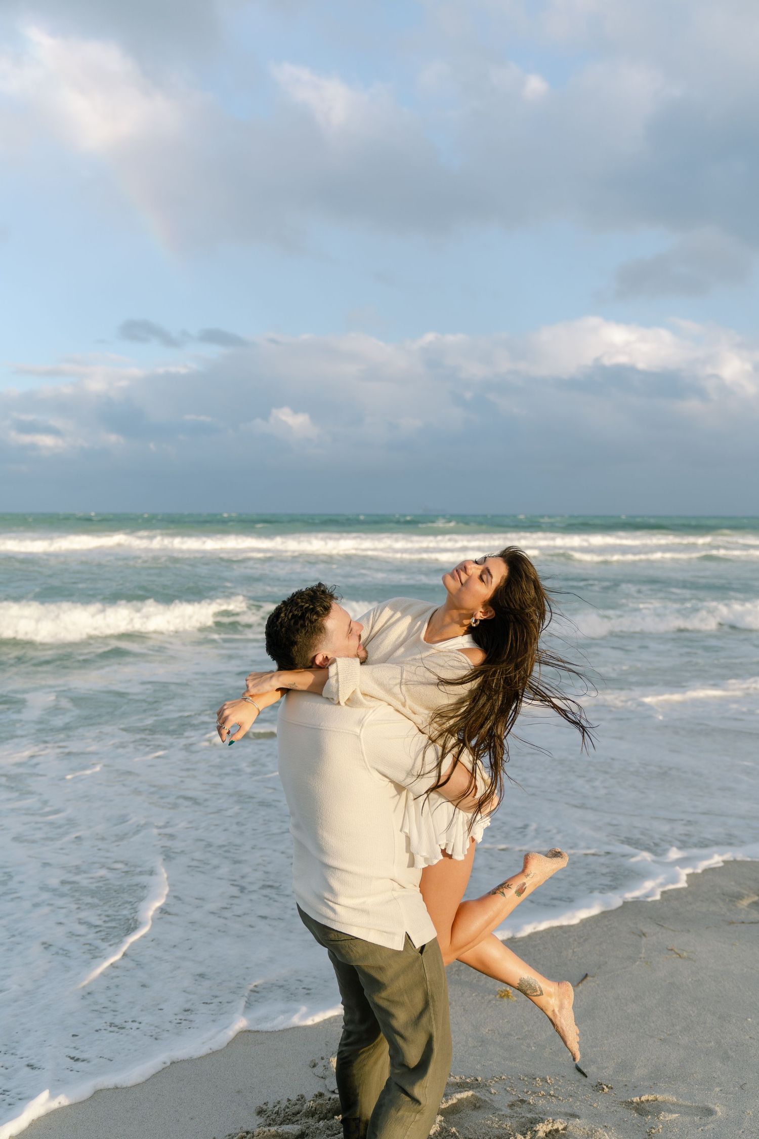 Romantic couple dancing and spinning together on a scenic beach with crashing waves in the background.