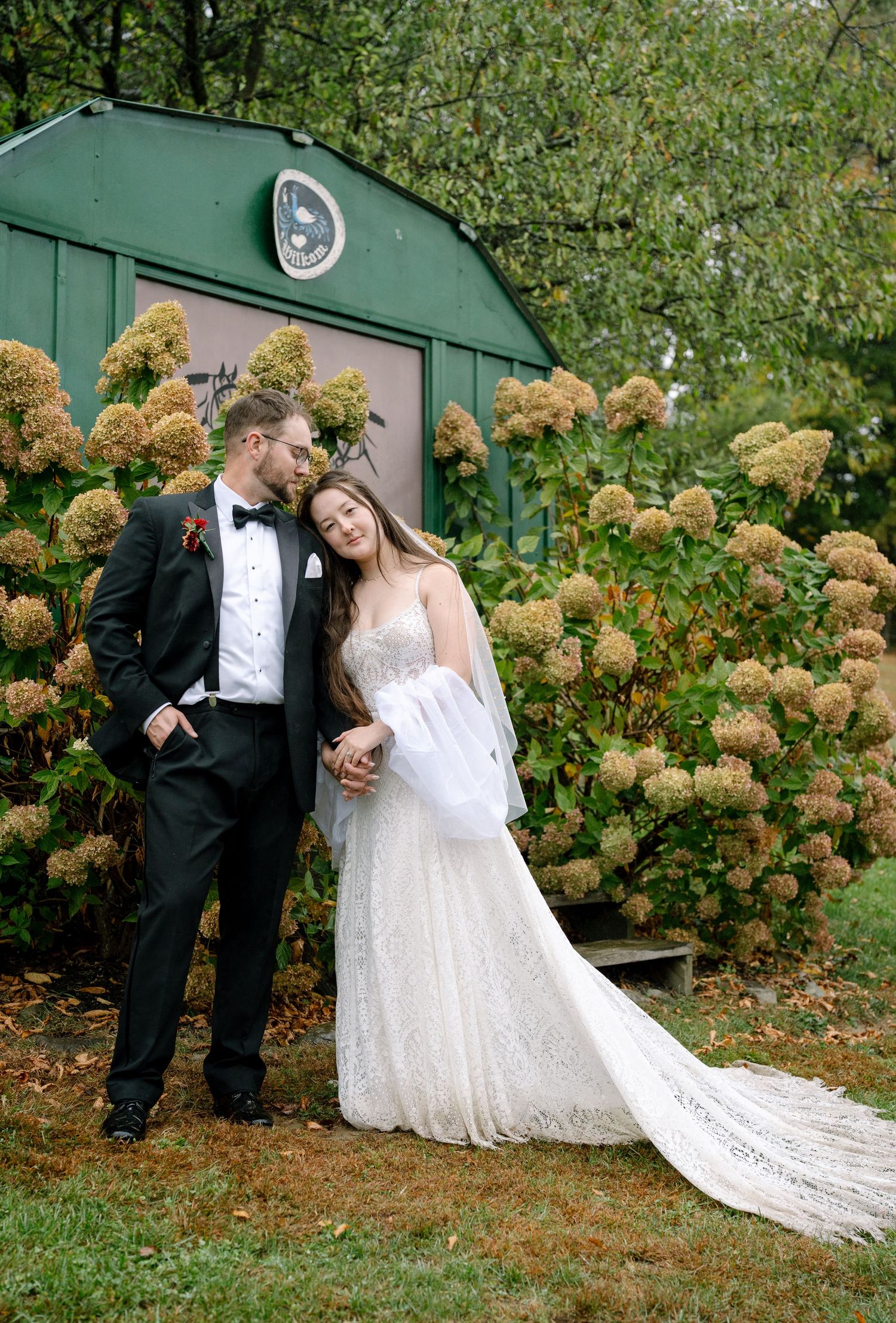 Wedding couple shares intimate moment near green wall with autumn hydrangeas in outdoor setting.