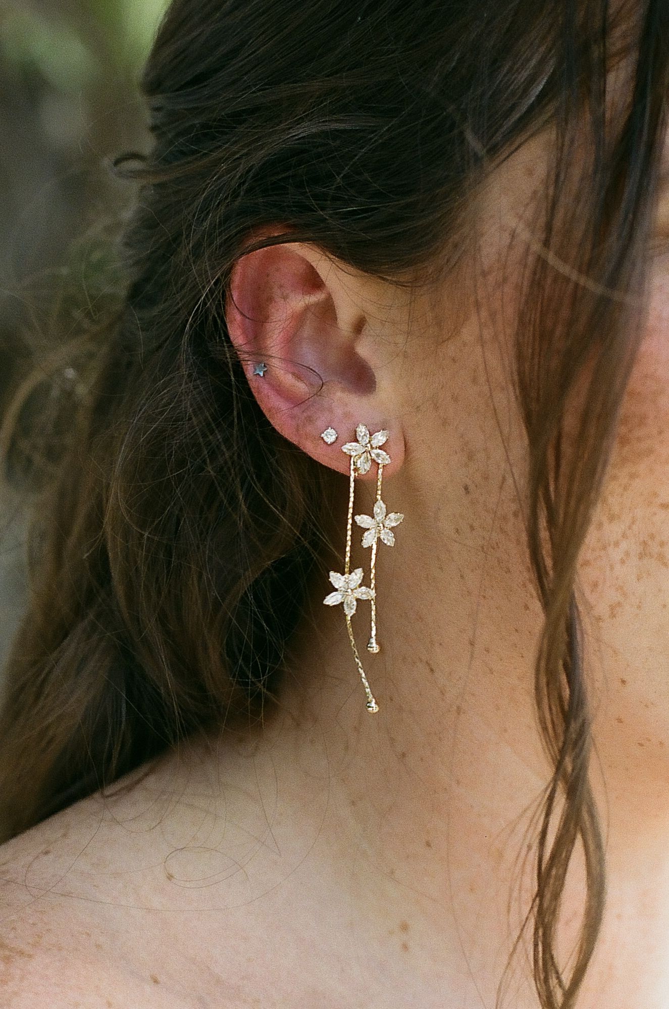 Close-up of a woman wearing elegant gold floral drop earrings with crystal details and delicate chain accents.