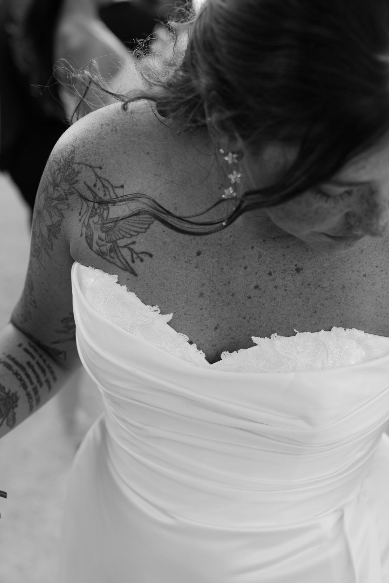 A close-up view of a bride's tattooed back in a white wedding dress.