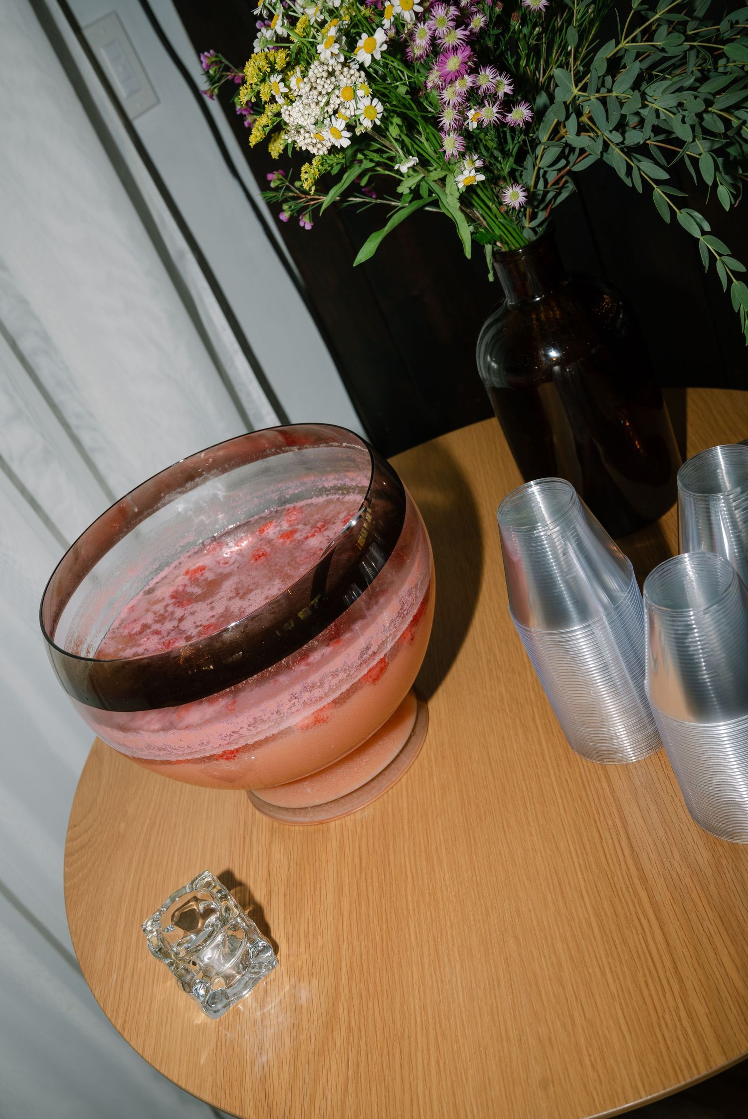 Pink cocktail in copper coupe glass on wooden table with wildflowers in background.