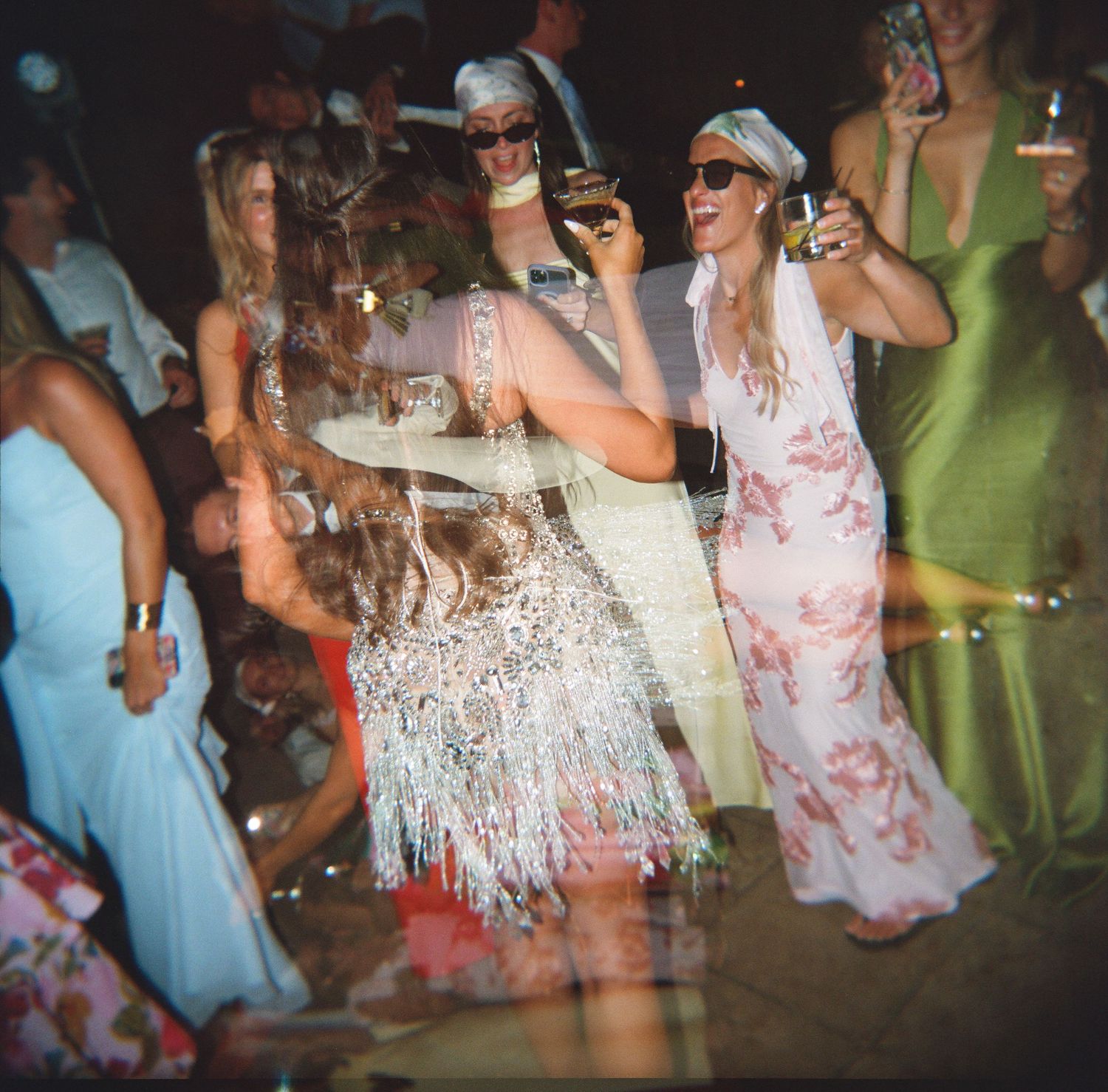 Guests in elegant dresses dancing and celebrating at a lively outdoor wedding reception at night.