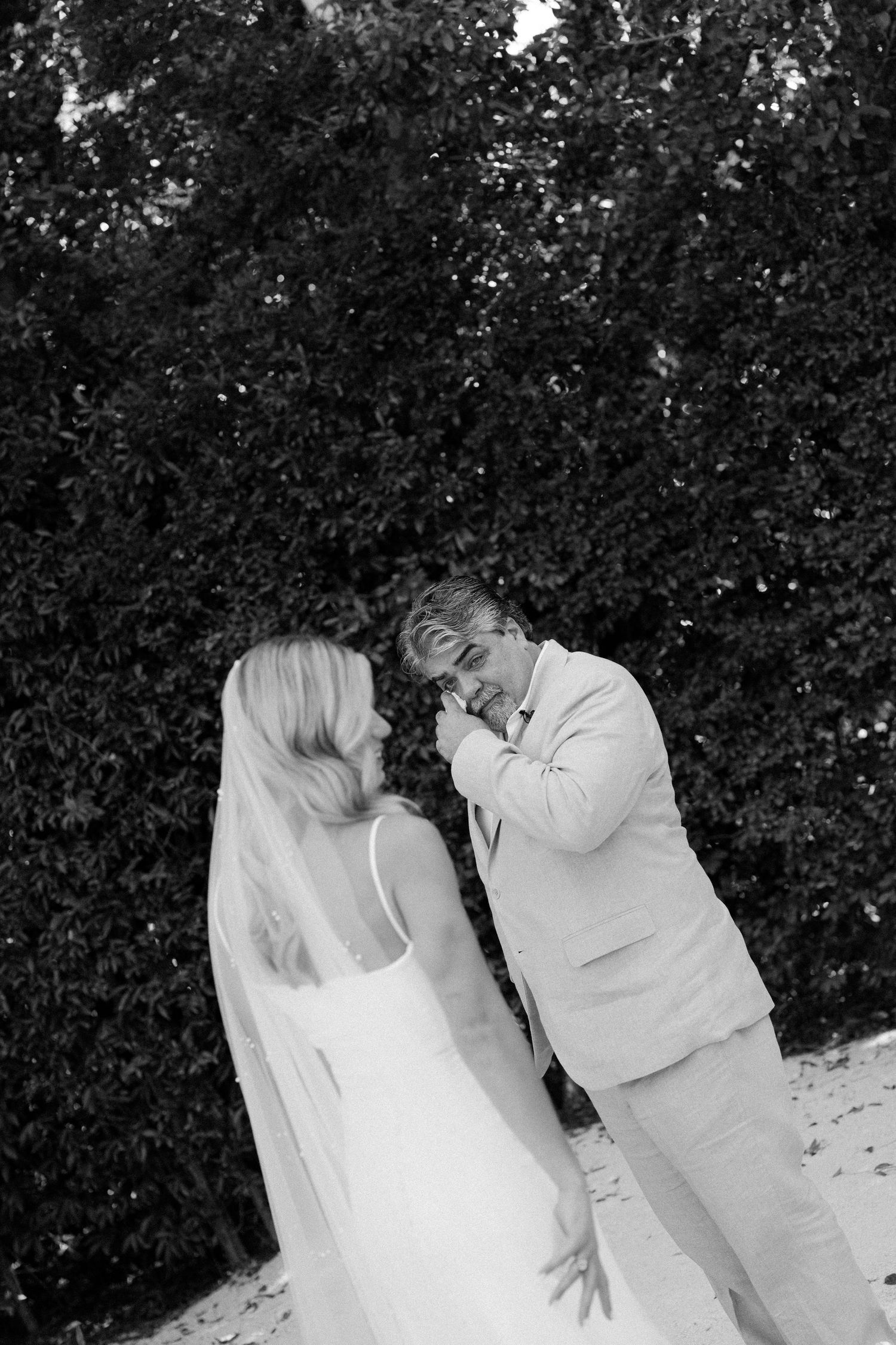 Black and white photo of an emotional first look moment between a bride and groom in front of greenery.