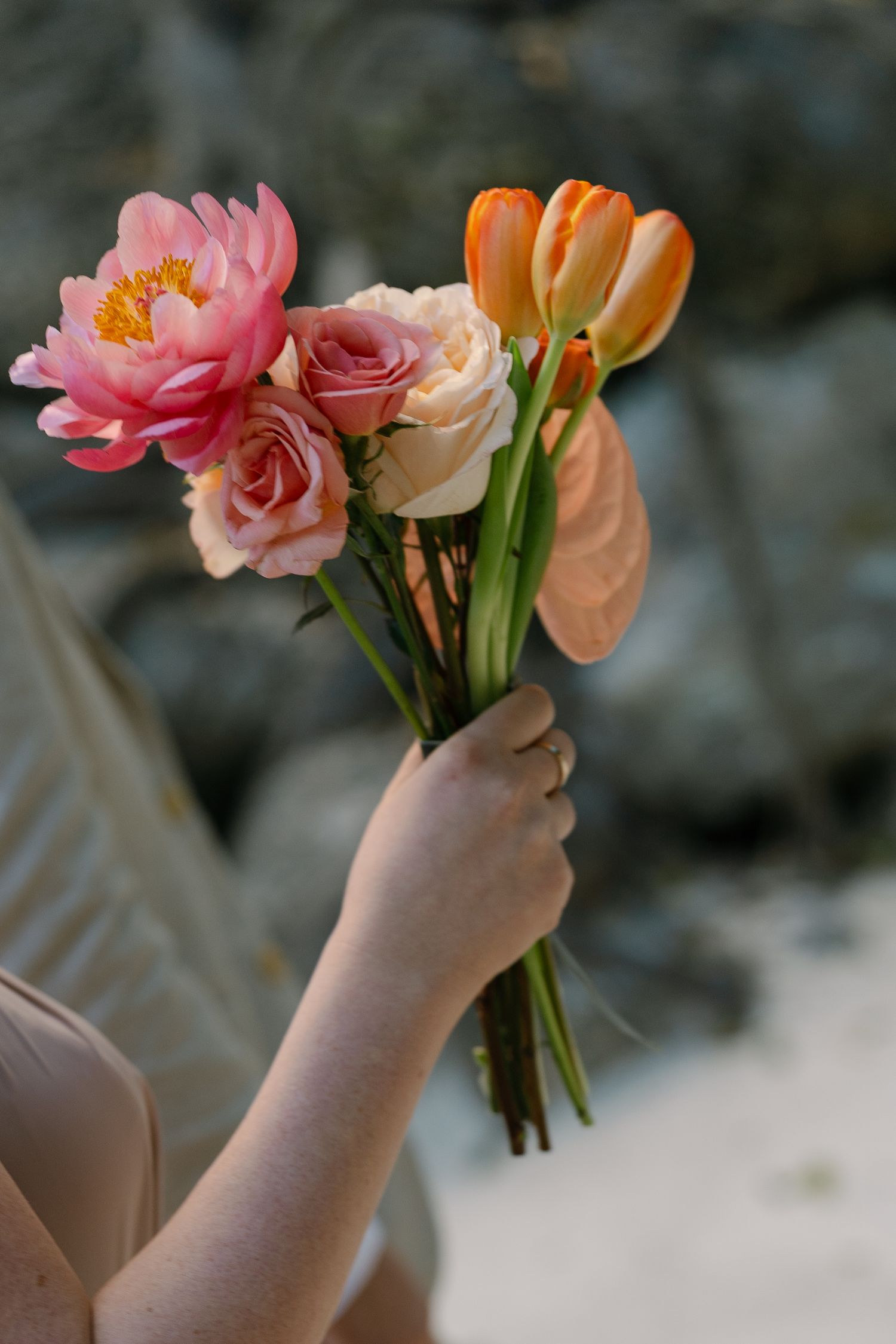 Close-up of hands holding delicate pink and orange flowers in soft focus.