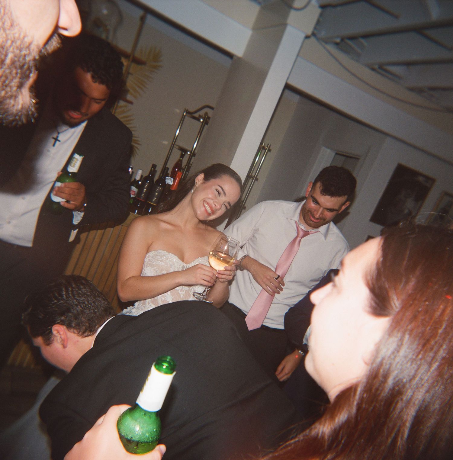 Bride in strapless gown socializes with guests holding drinks at lively wedding reception party.