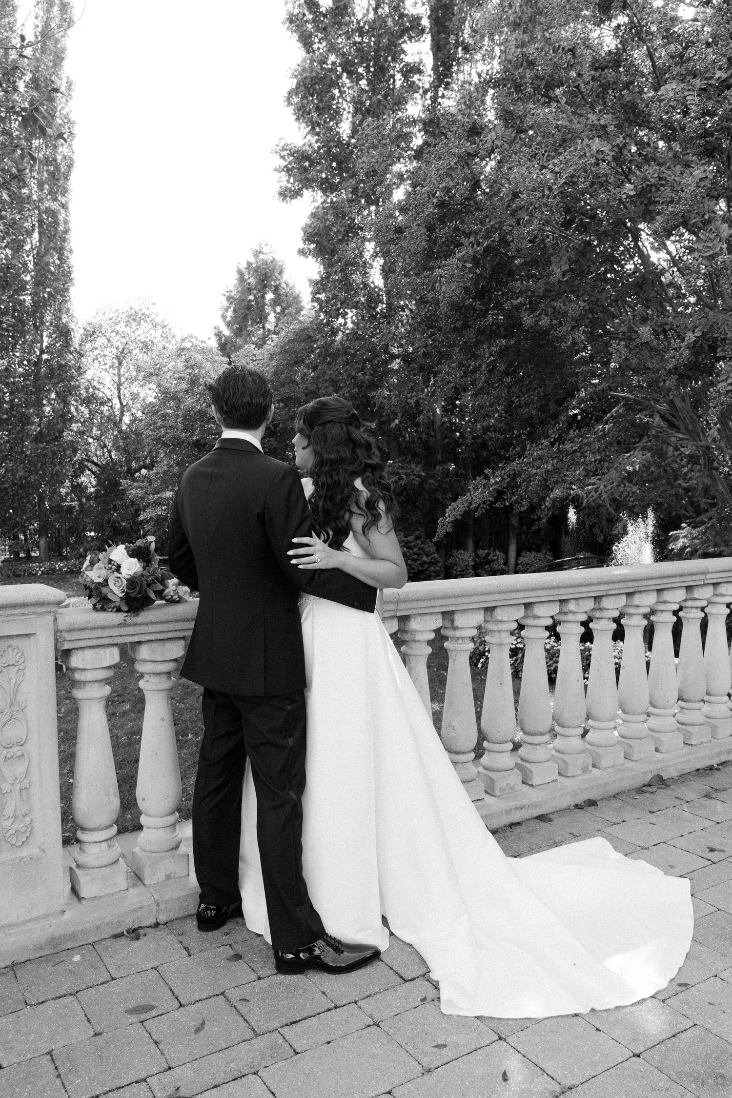 Wedding couple poses on stone balcony with ornate balusters in black and white sequence.