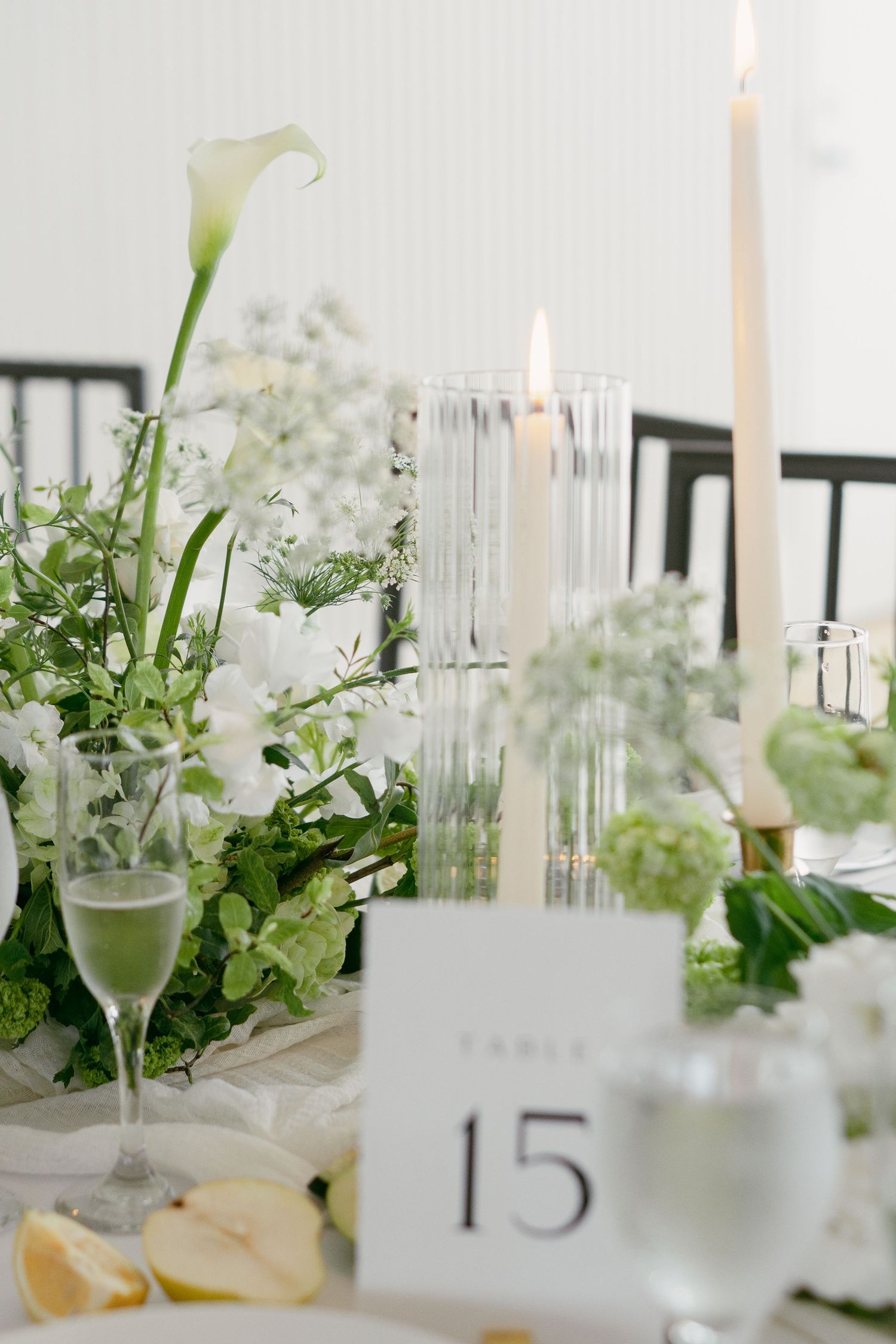 Elegant wedding table setting with white calla lilies, candles, and table number 15 amidst delicate floral arrangements.