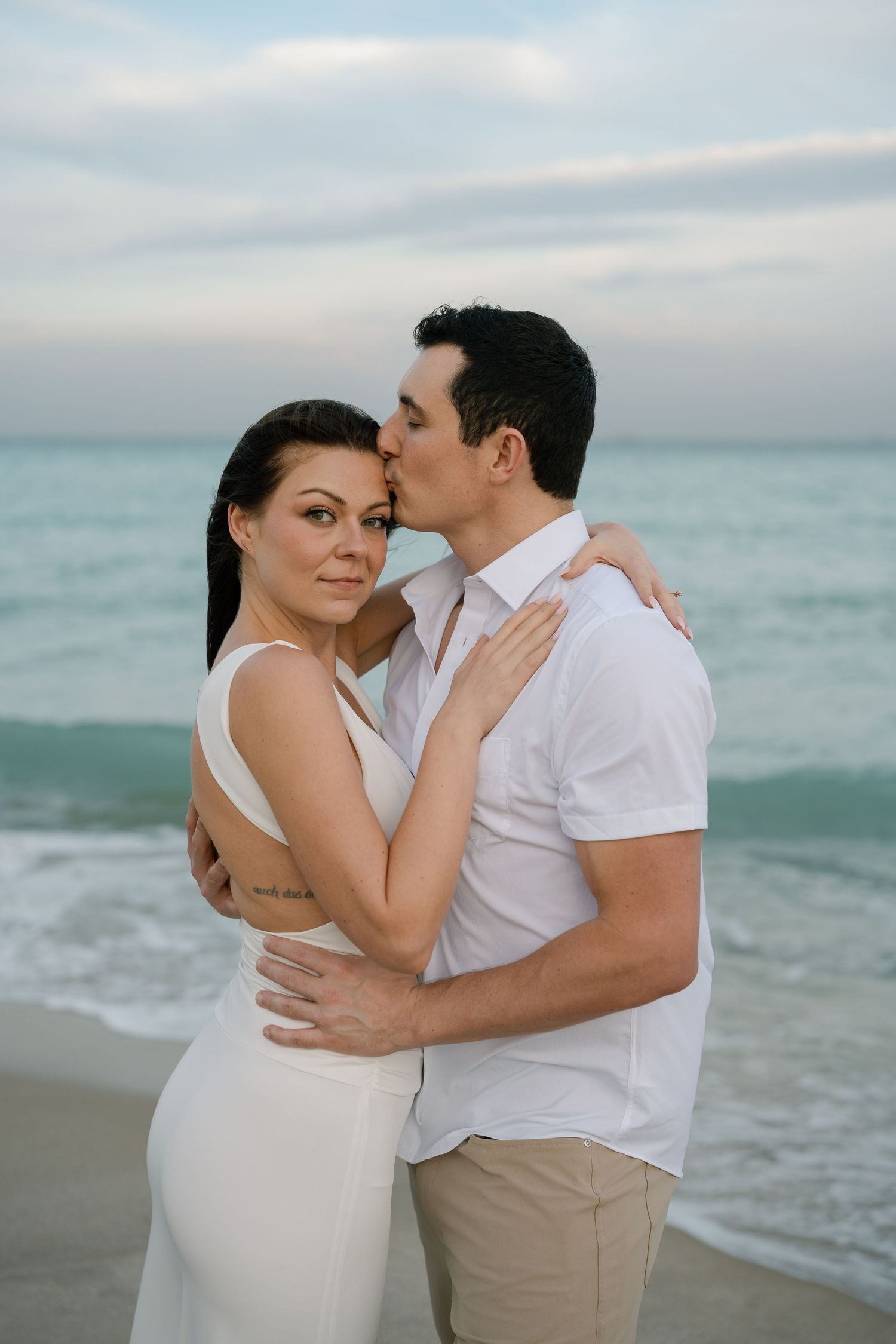 Romantic beach portraits of couple embracing with ocean waves in background.
