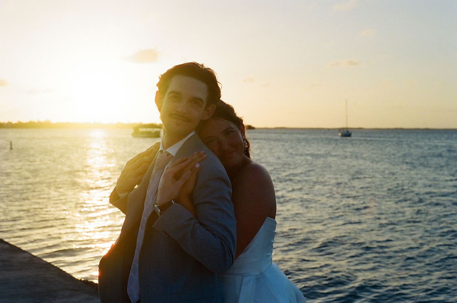 A couple embracing and looking out at the sunset over the ocean.