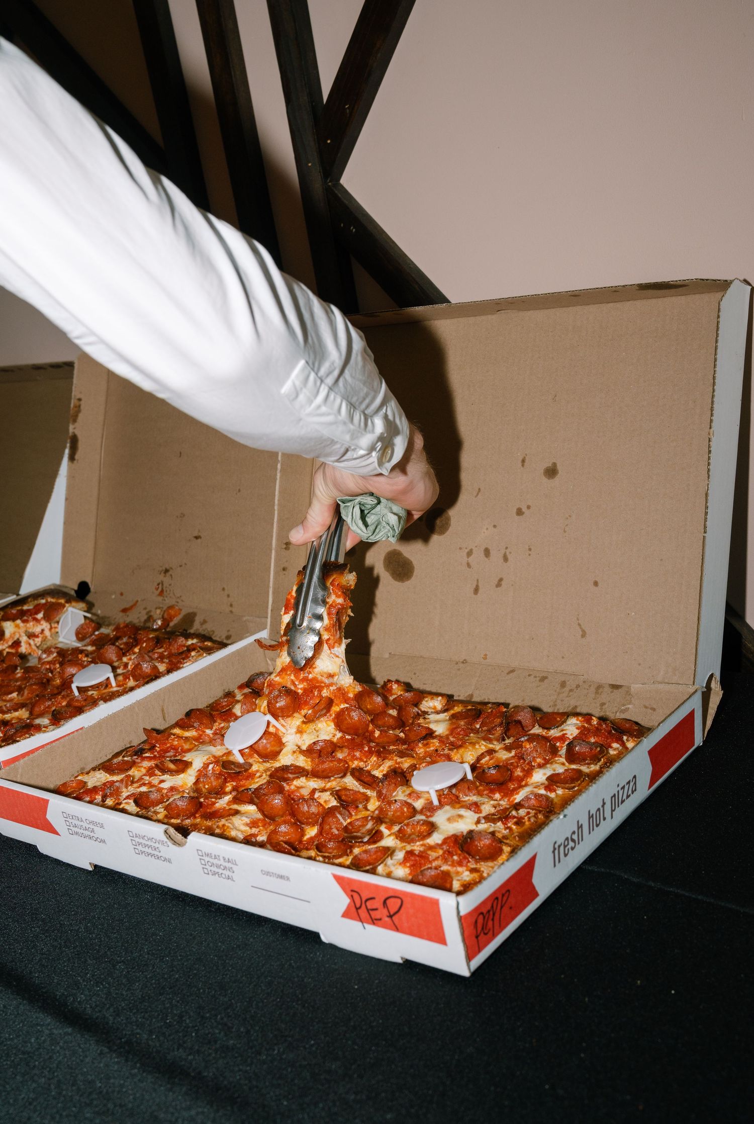 Multiple hands reach into a large pizza box grabbing slices at a wedding reception.