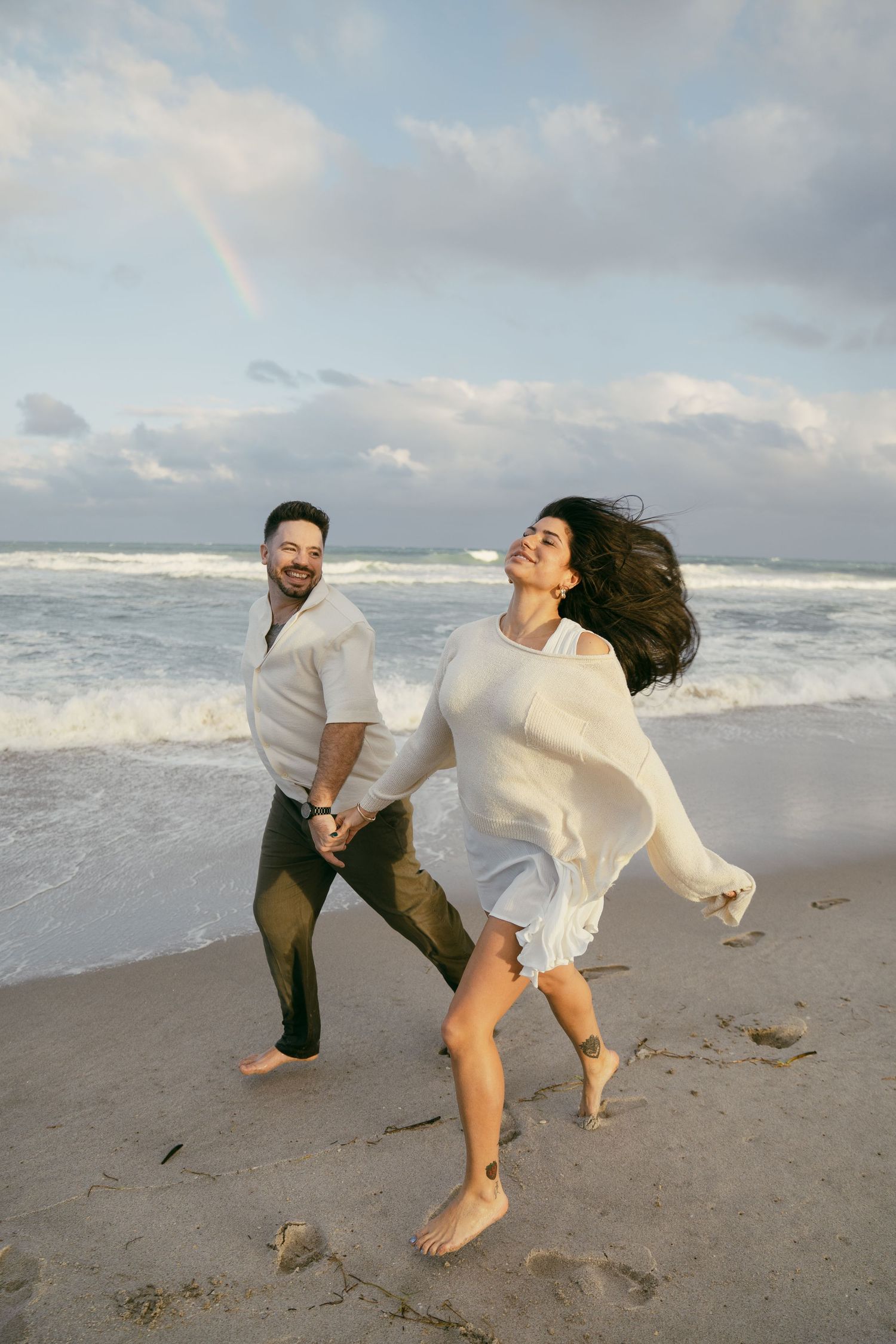 A joyful photoshoot set on the beach showing playful movement and energy as the waves roll in behind.