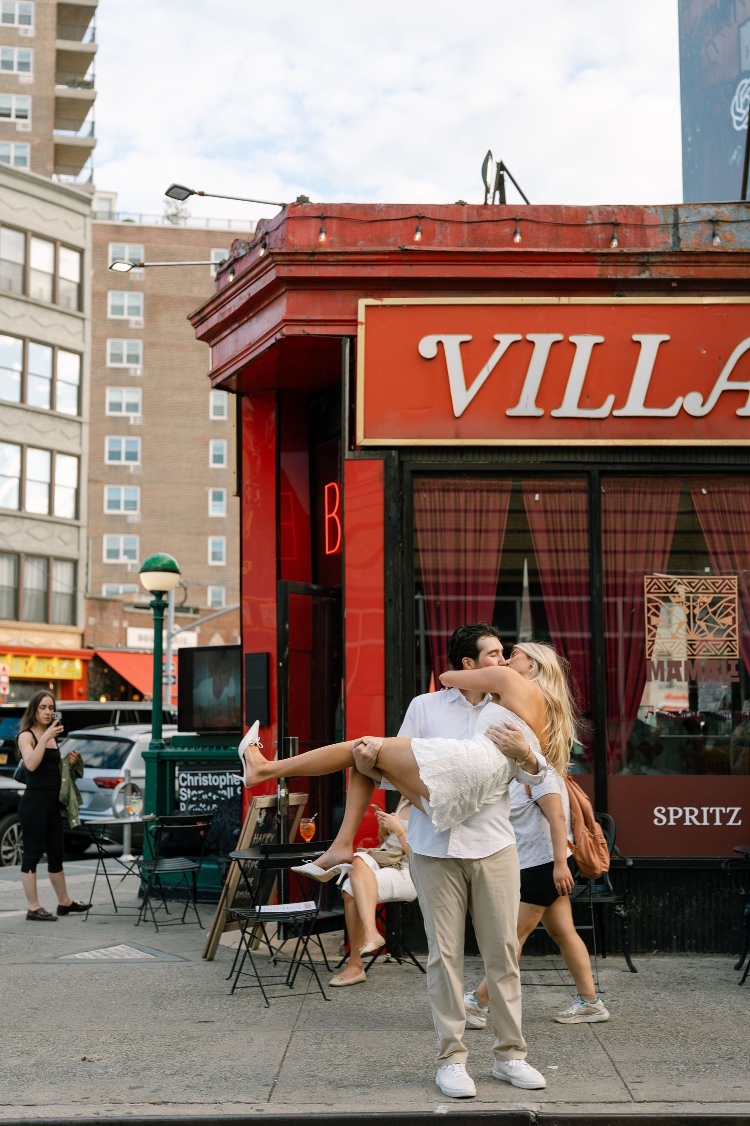 Man lifting woman outside Villa restaurant on a busy New York City street corner.