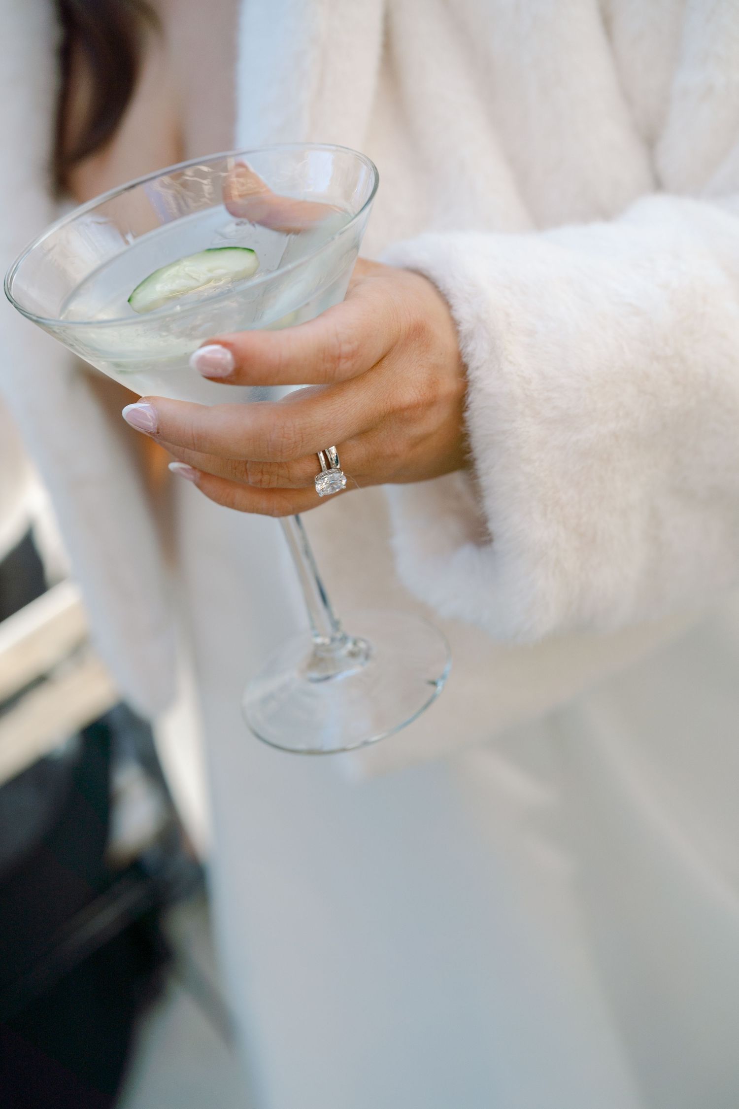 A person's hand holding a glass of clear liquid, likely a cocktail.