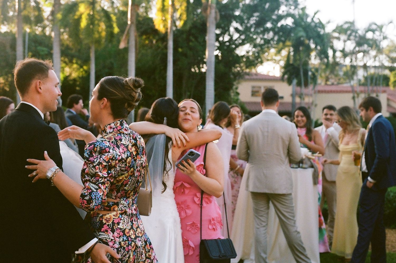 Wedding guests dancing and embracing outdoors at a tropical garden reception celebration.