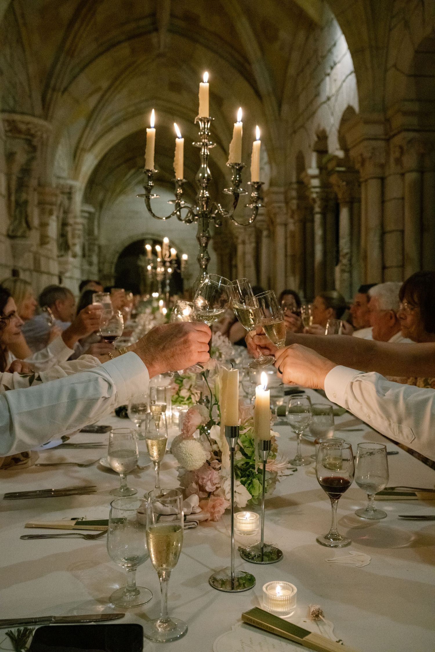 Elegant candlelit wedding dinner toast in a historic stone archway venue with guests raising champagne glasses.