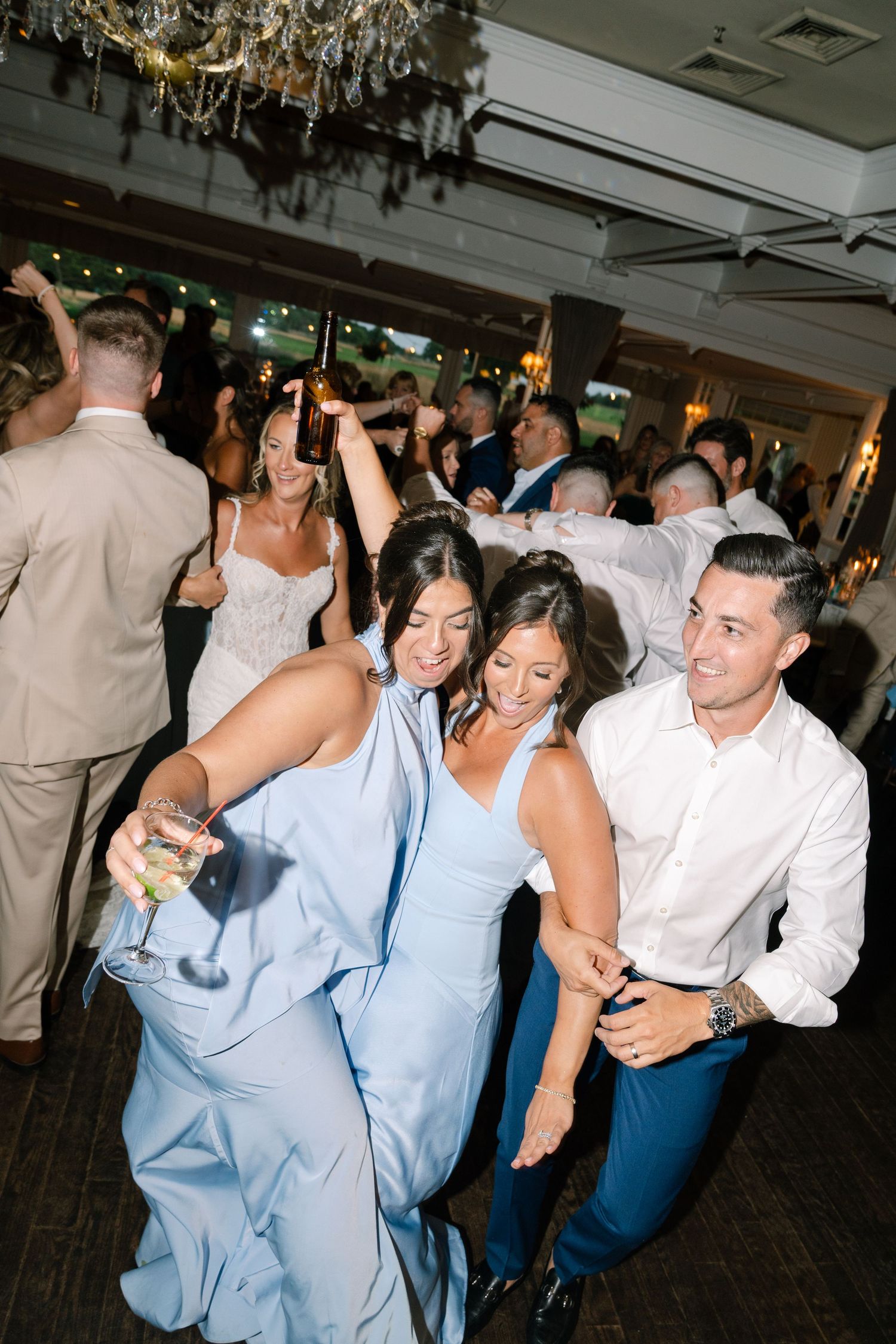 Guests dancing at wedding reception, bridesmaid in light blue dress holding champagne glass.