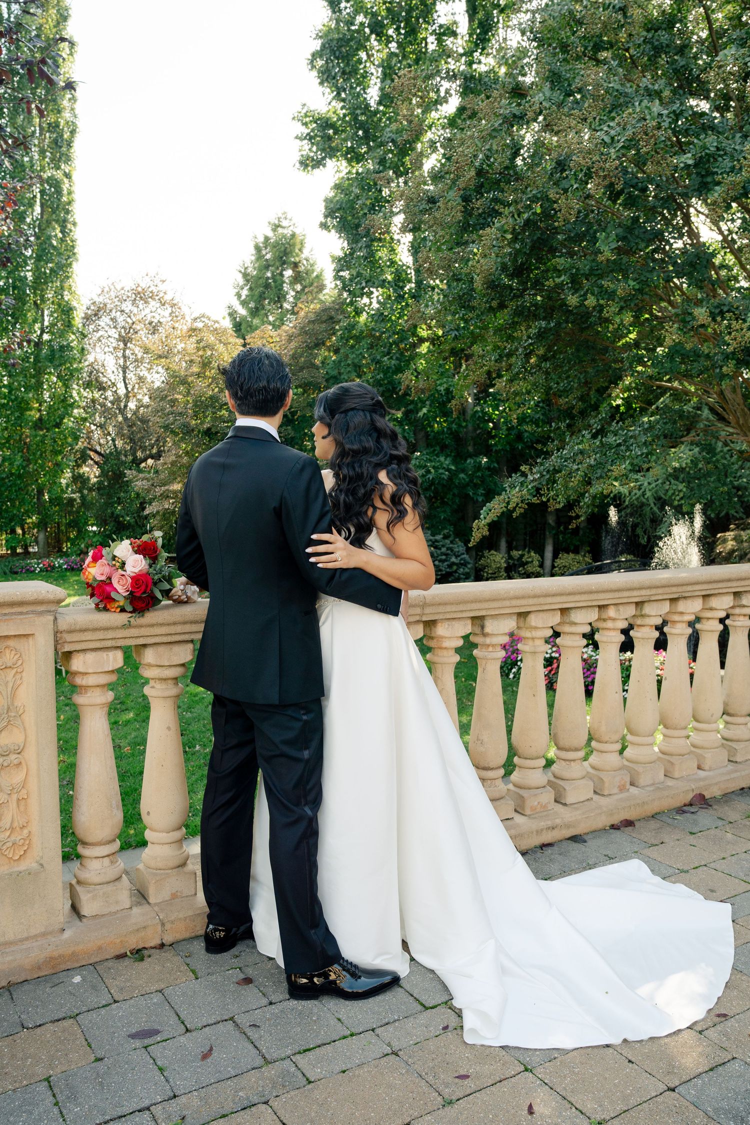 A couple shares an intimate moment on a stone balcony overlooking a scenic garden landscape.