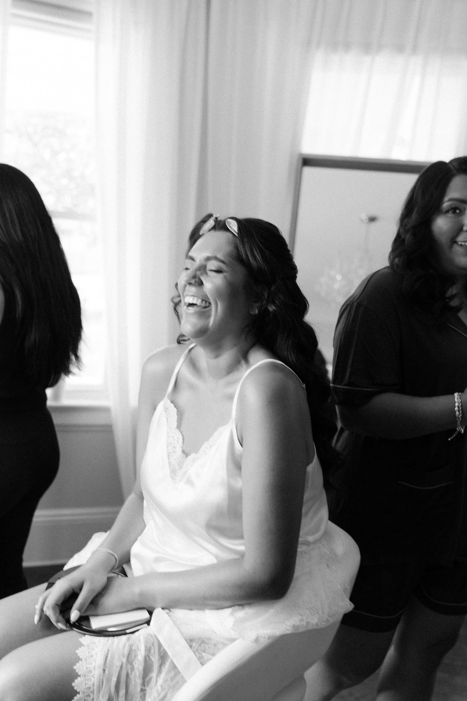 Black and white candid photo showing joyful laughter during wedding preparations.