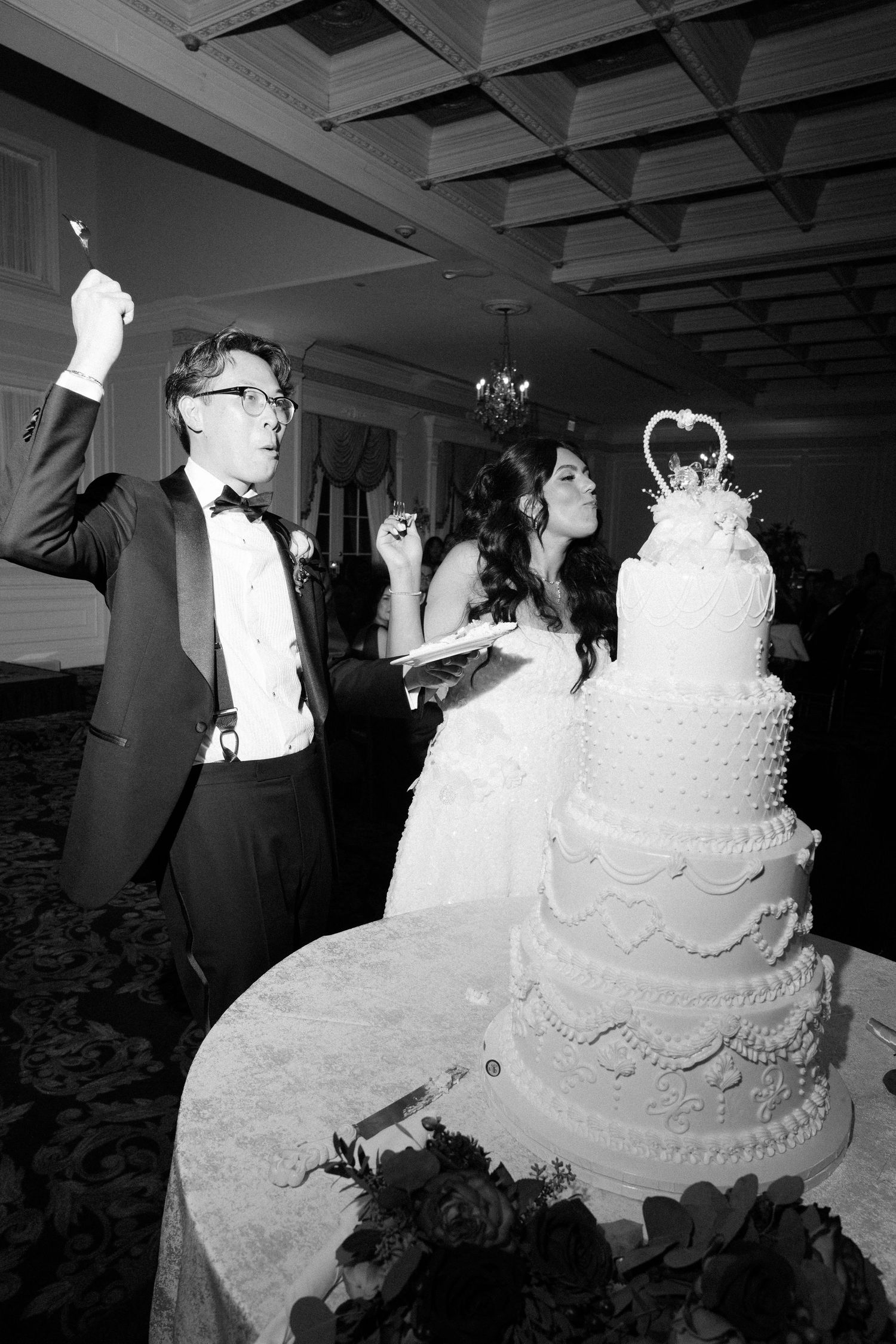 Wedding reception features elegant tiered white cake with ornate decorative details.