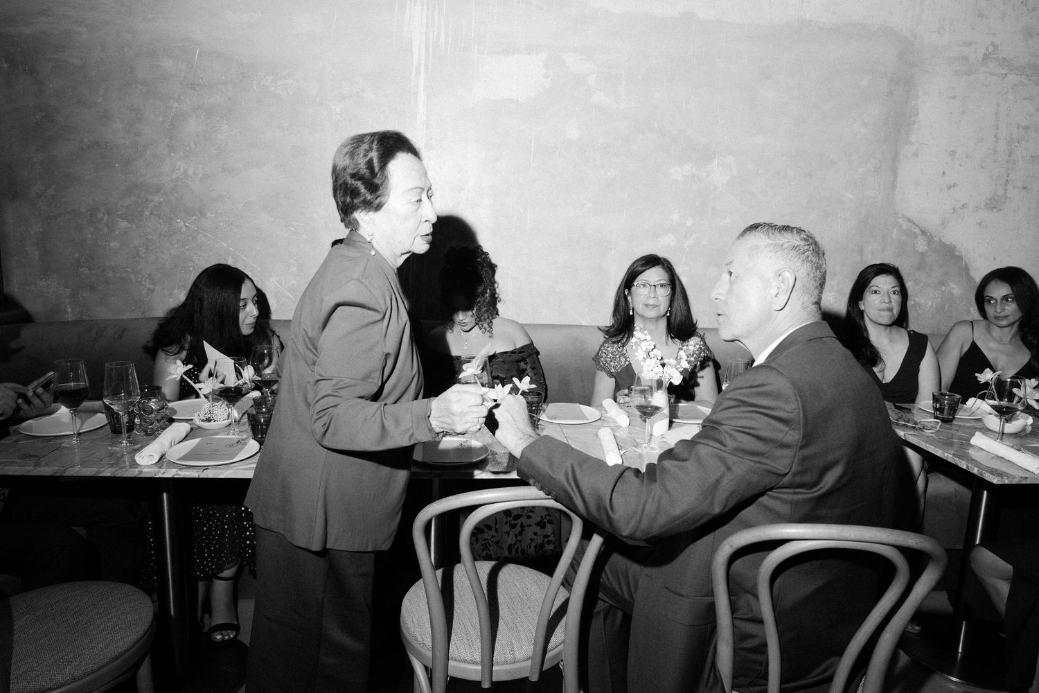 Black and white candid shots of people socializing at tables during an indoor gathering.