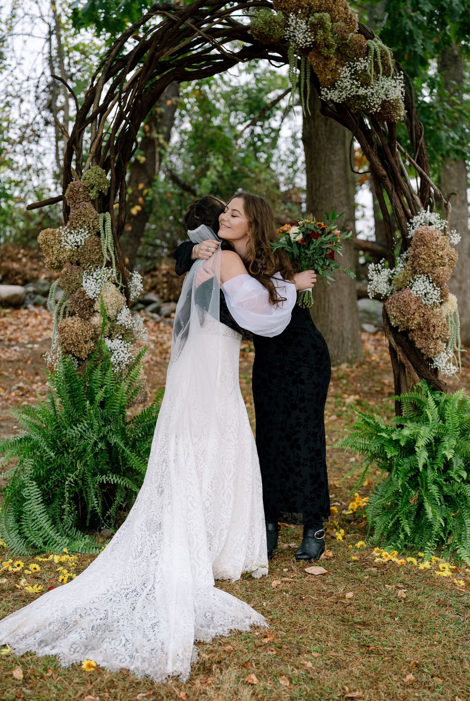 A couple in wedding attire shares a romantic moment in a wooded outdoor setting with autumn leaves and ferns.