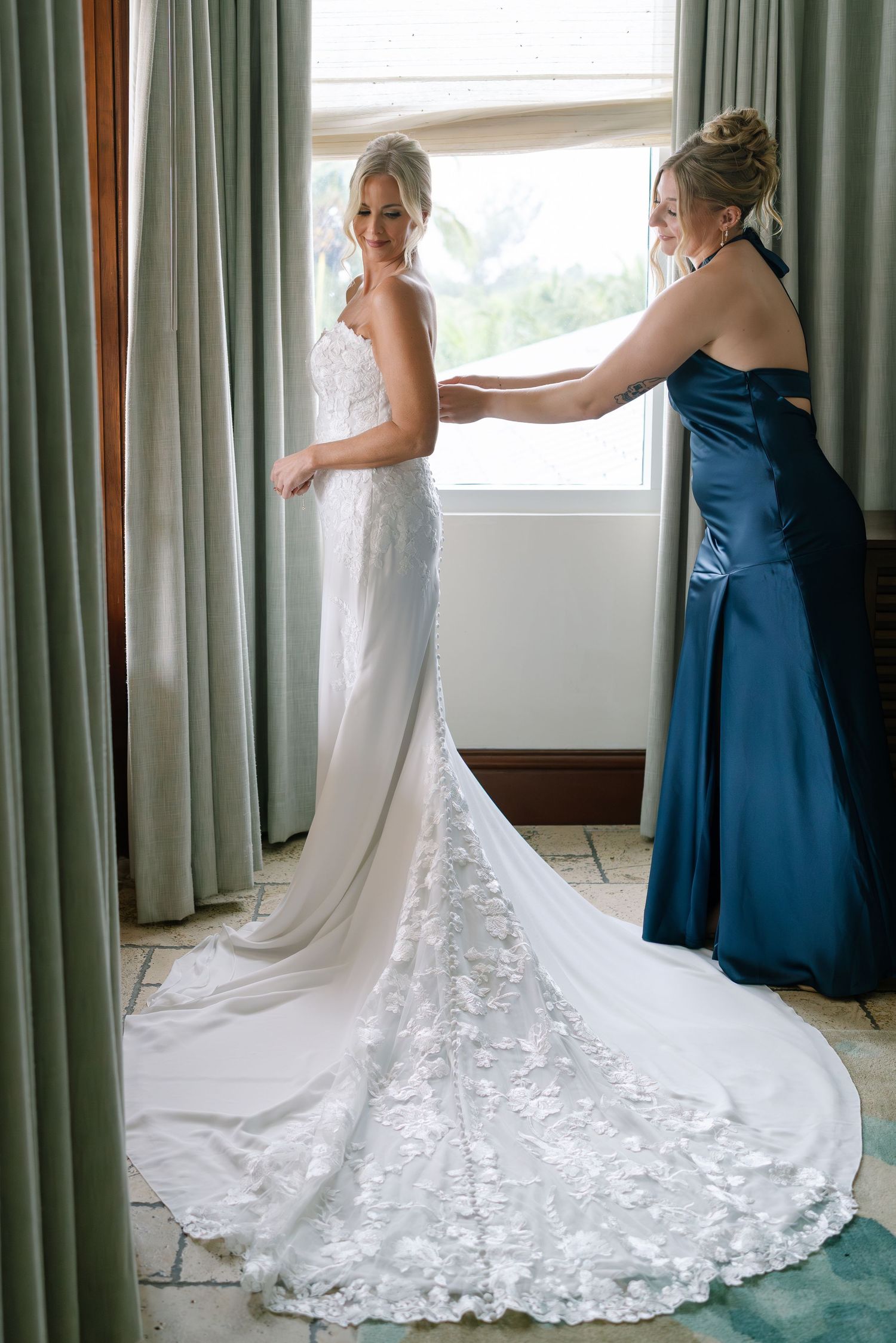 Wedding dress fitting scene with flowing lace train and navy blue bridesmaid dress.
