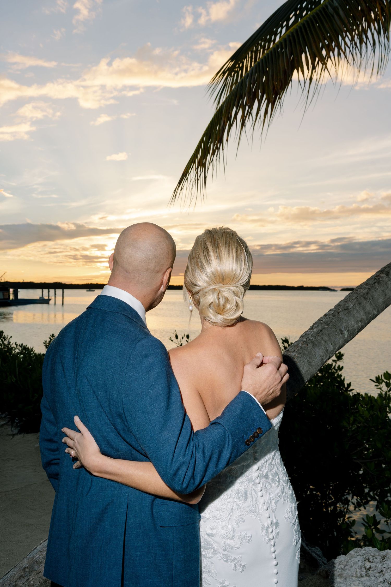 Couple embraces while watching sunset over tropical waters.