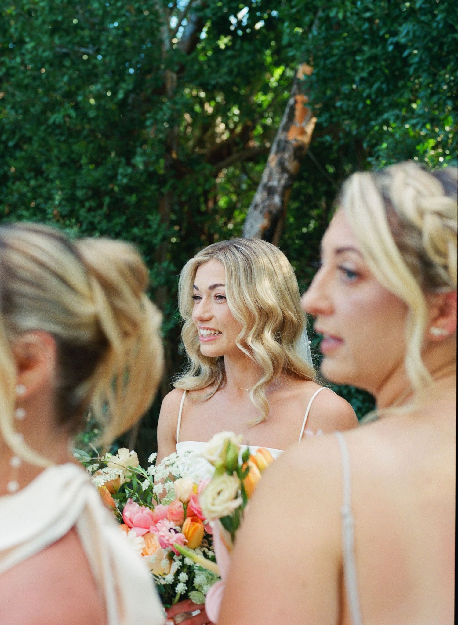 Bridesmaids in light colored dresses holding colorful bouquets outdoors in a garden setting.