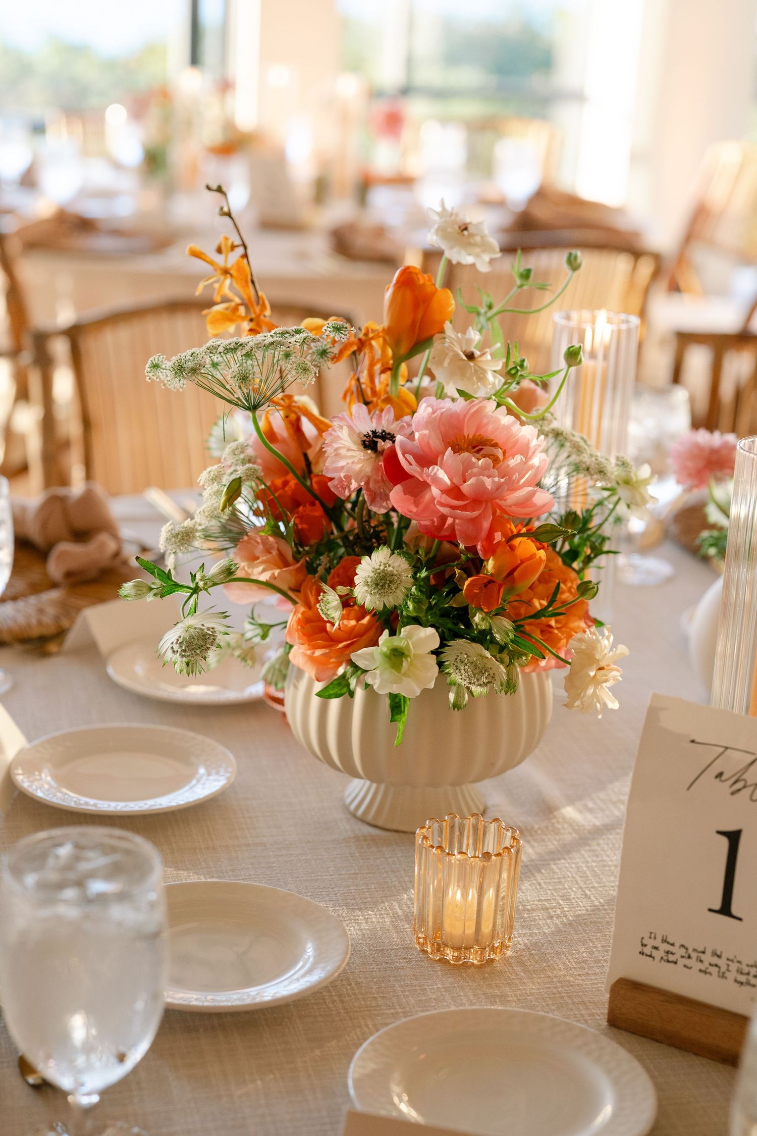 Elegant coral and orange floral centerpiece in white ribbed vase on wedding reception table.