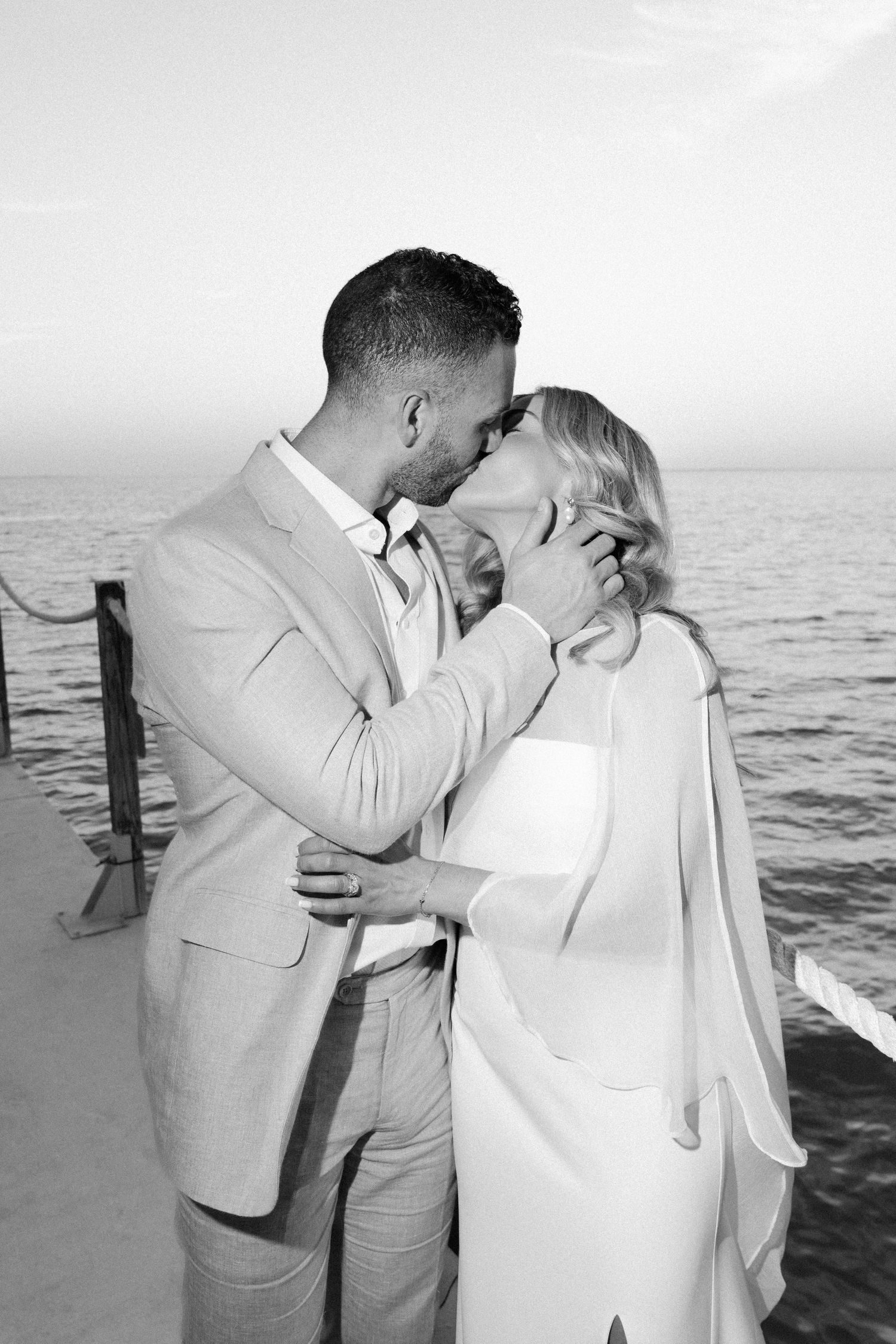 Romantic black and white portrait of a couple embracing by the ocean.