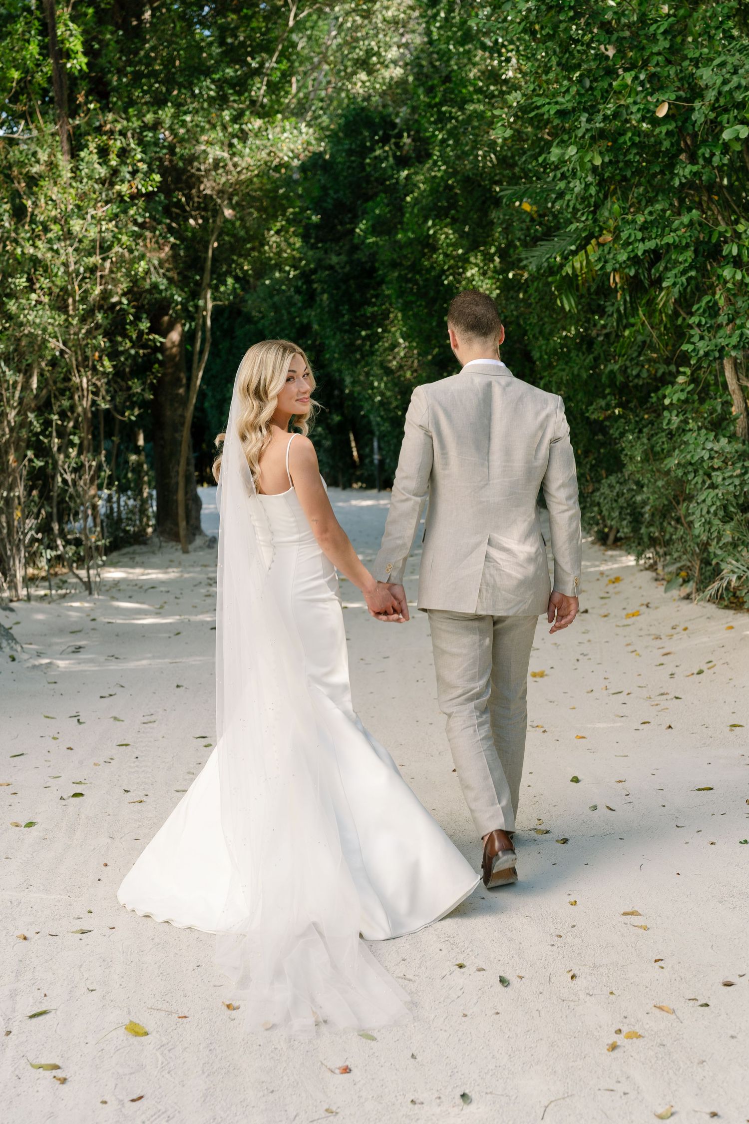 Newlyweds walking hand in hand through a lush garden pathway.