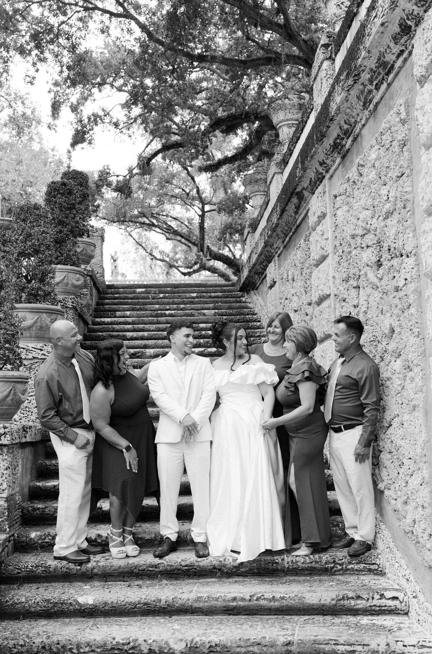 A vintage black and white photograph of a group posing together on stone steps near an ivy-covered wall.