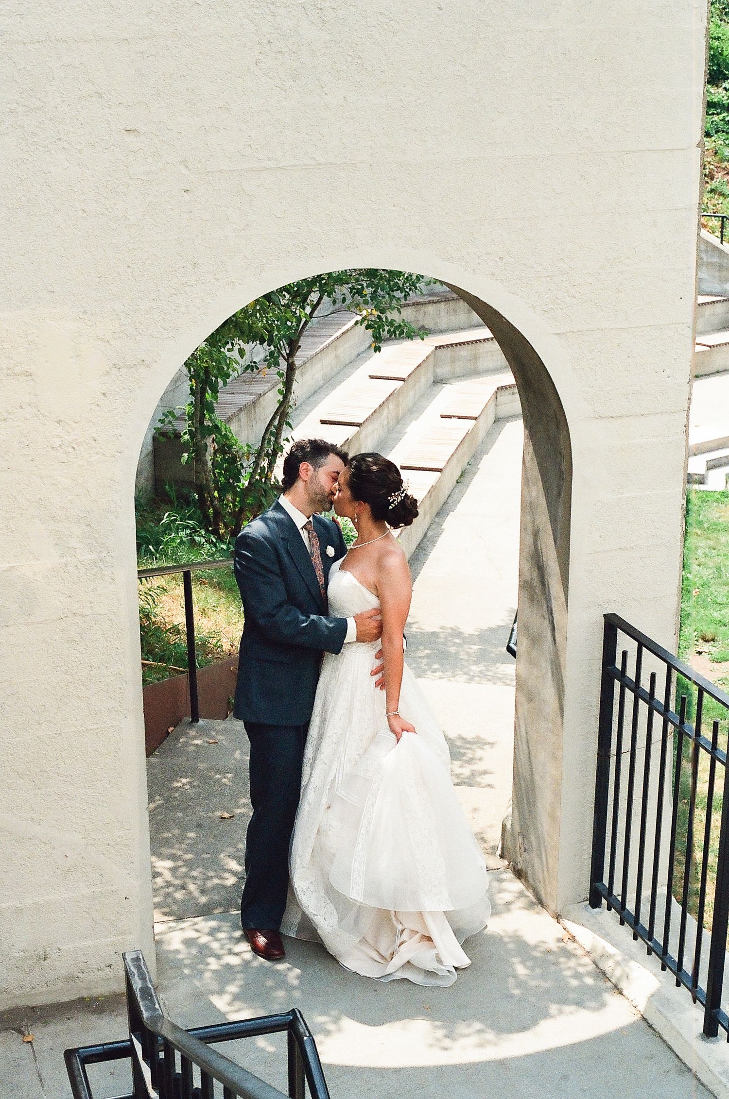 A tender moment captured under a stone archway on a sunny wedding day.
