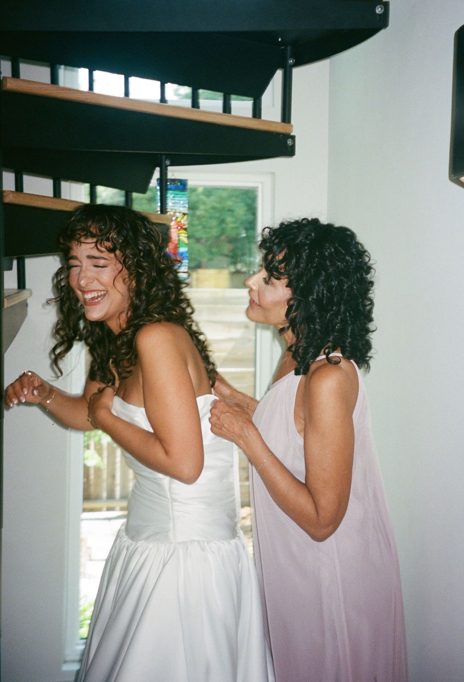 Candid moment of joyful laughter between bride and bridesmaid with matching curly hair.