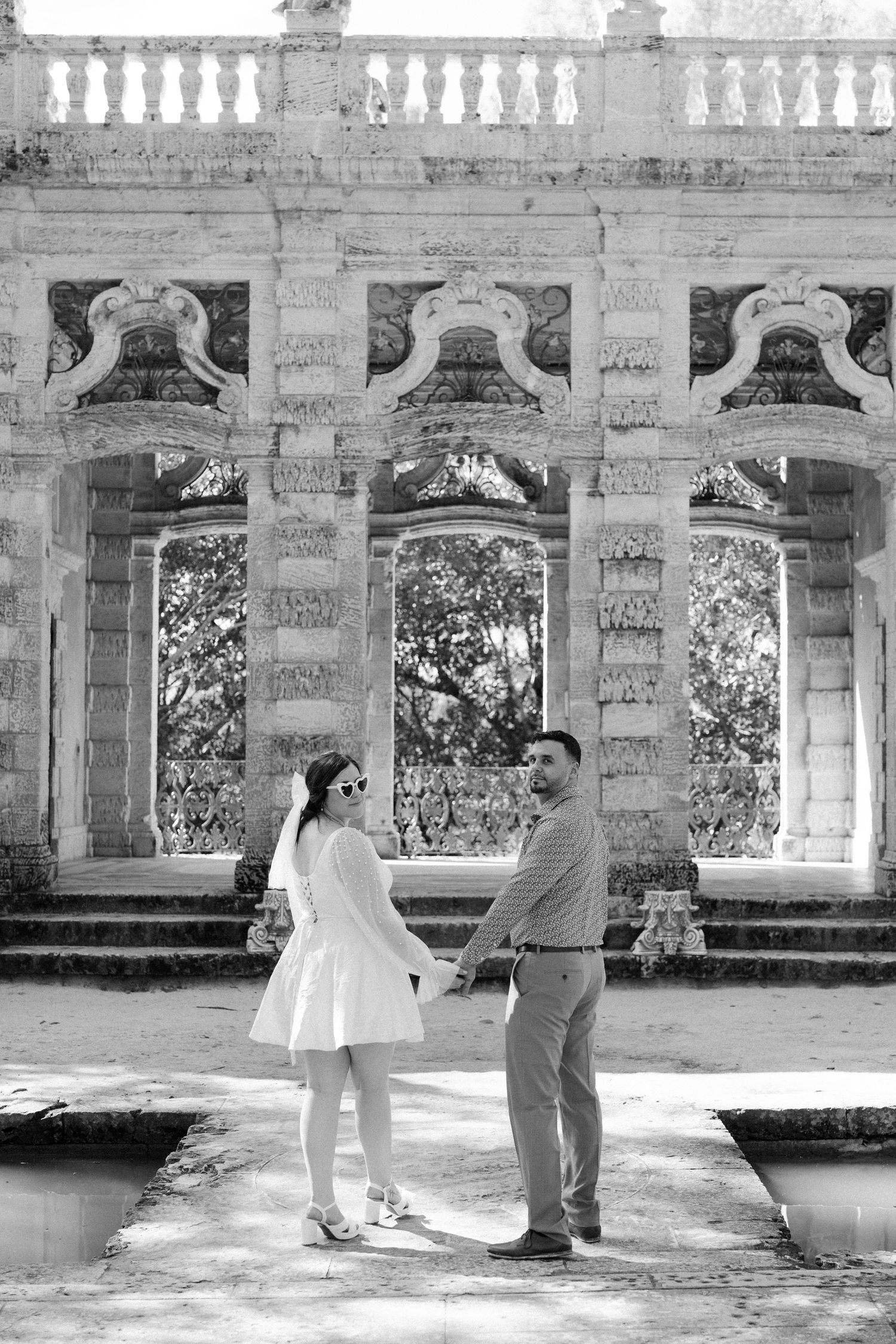 Black and white photo of a couple dancing in front of a classical stone colonnade.