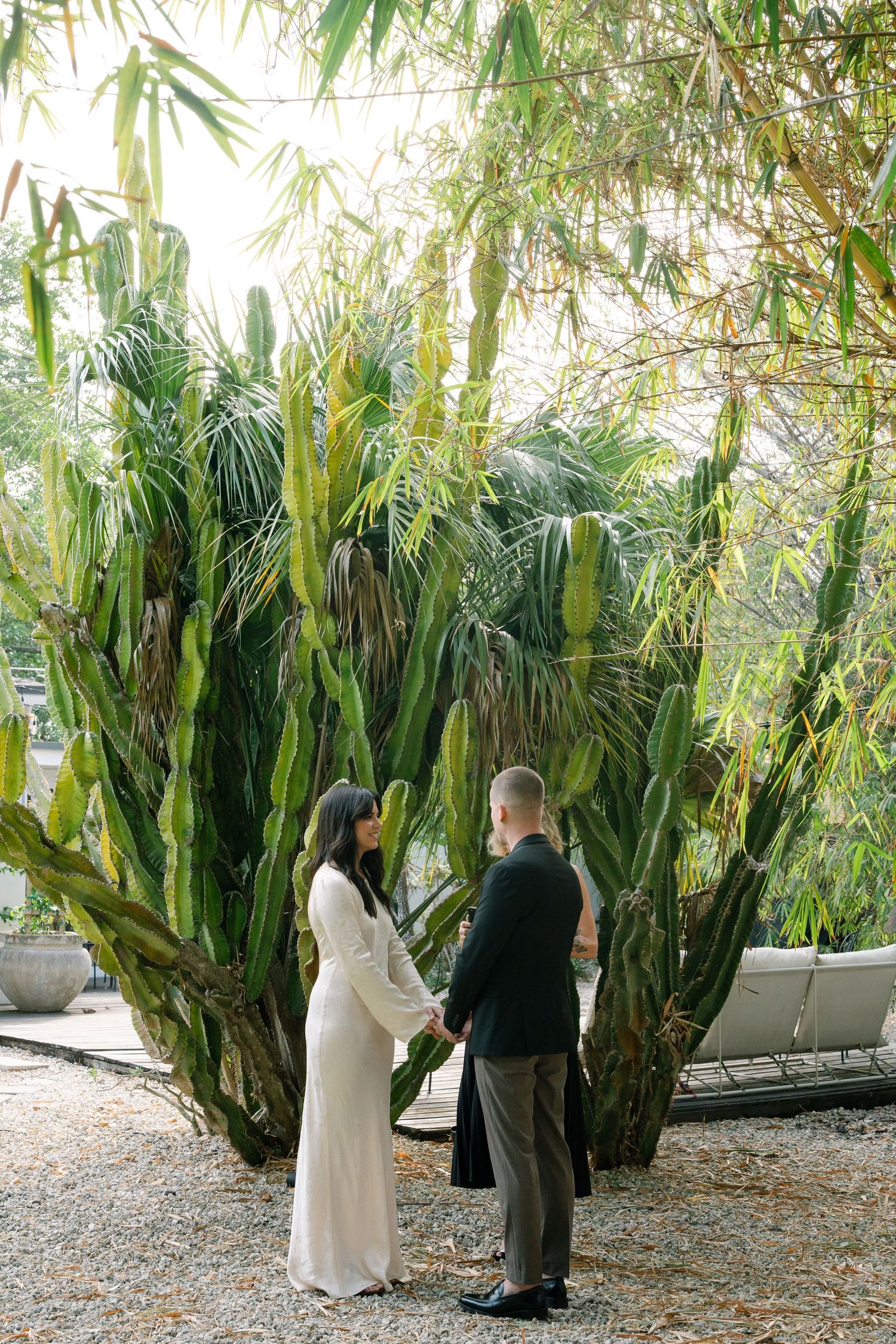 A couple shares a first look moment surrounded by lush palm trees and tropical foliage in a garden setting.